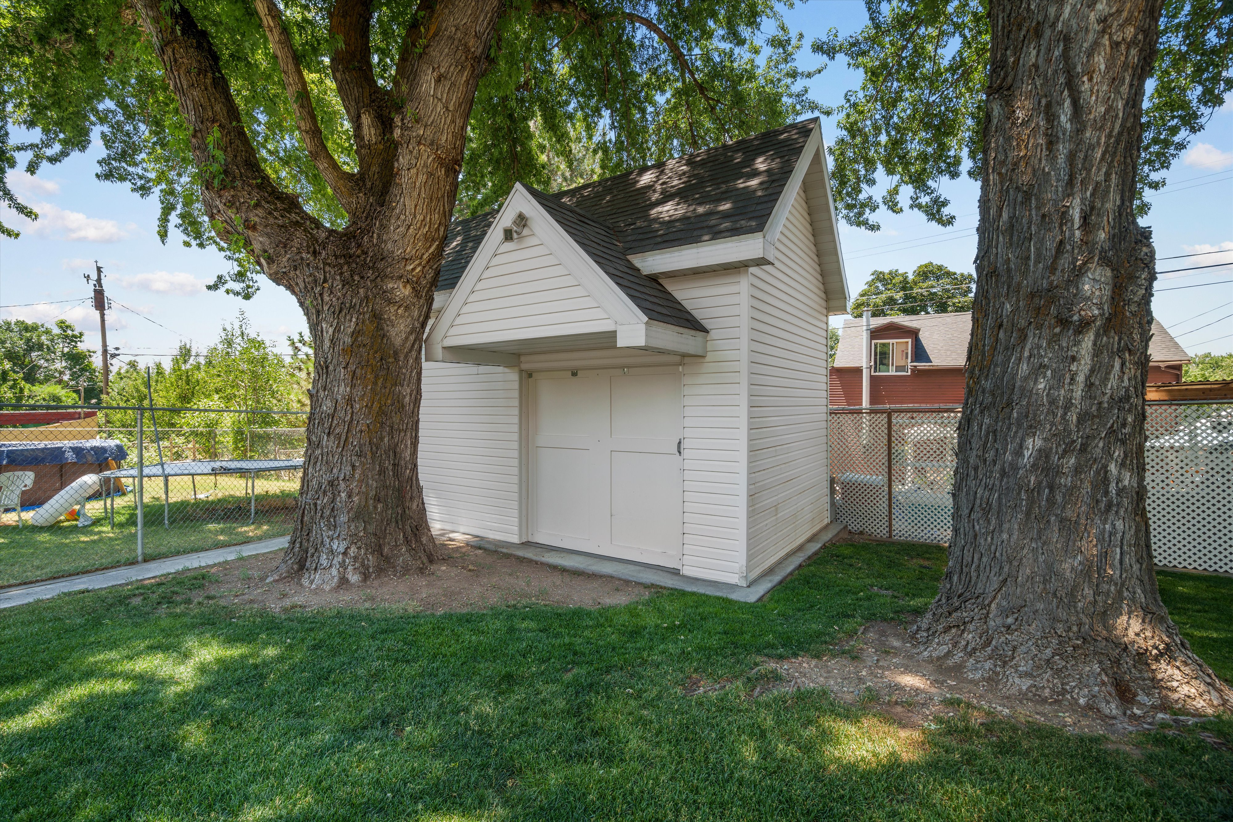 White storage shed featuring a pitched roof, double doors, and a small overhang