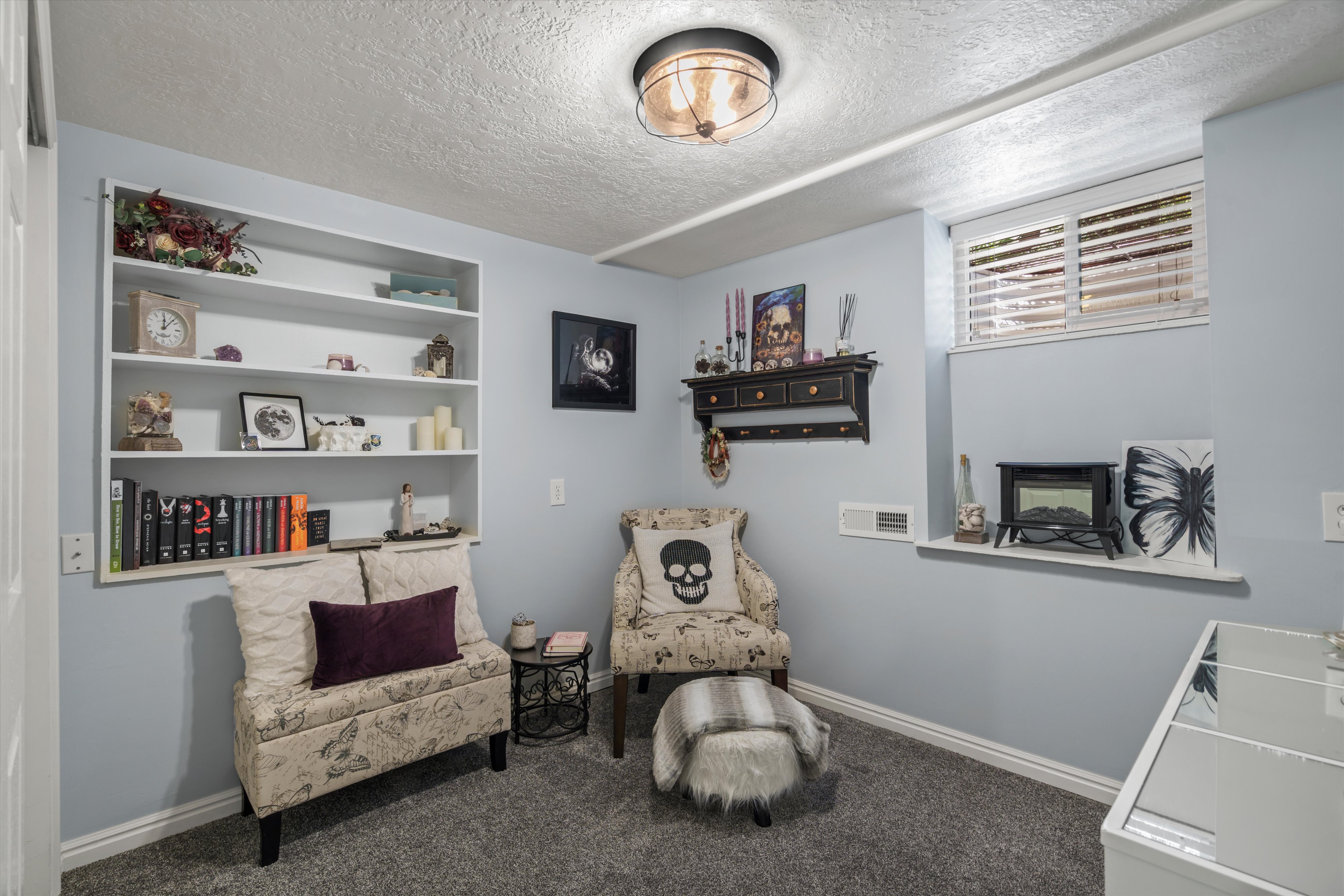 Light blue walls complement the textured gray carpeting in this room featuring a built-in shelving unit, a window with blinds, and a circular ceiling light
