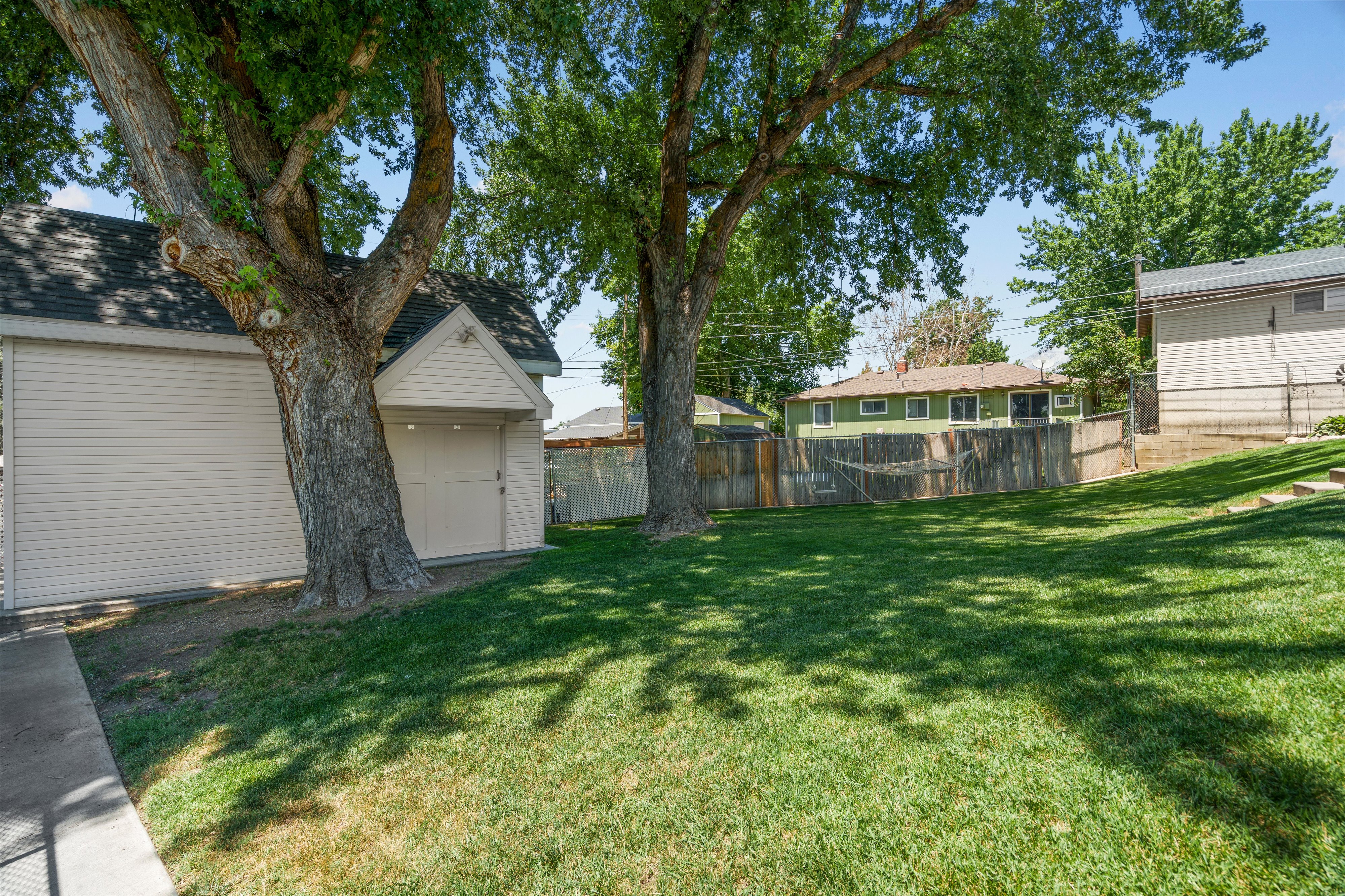 Expansive backyard featuring a manicured lawn, mature shade trees, and a detached structure with siding