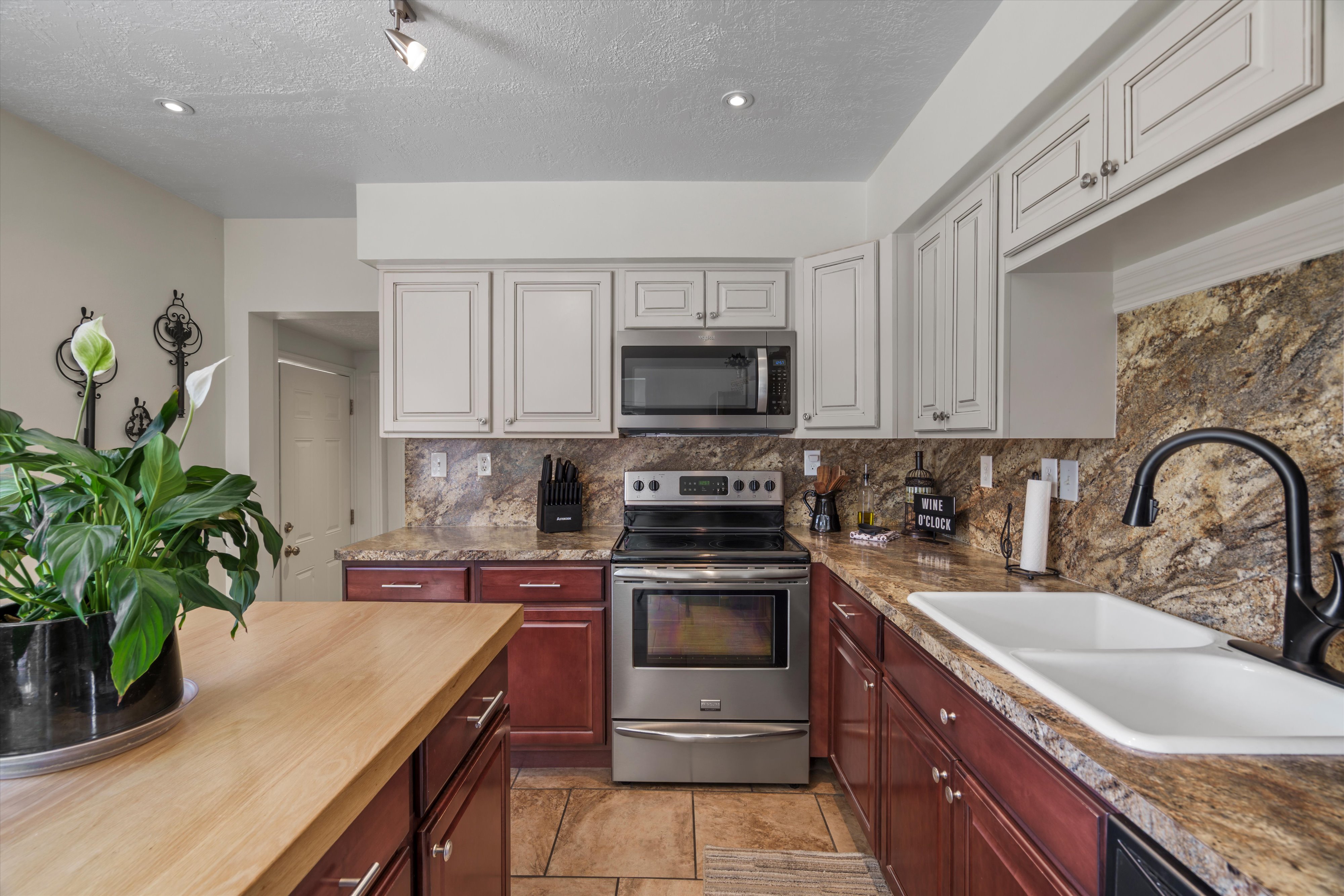 Kitchen featuring two-tone cabinetry, stainless steel appliances, a double basin sink with a matte black faucet, and a large wood-finish countertop island