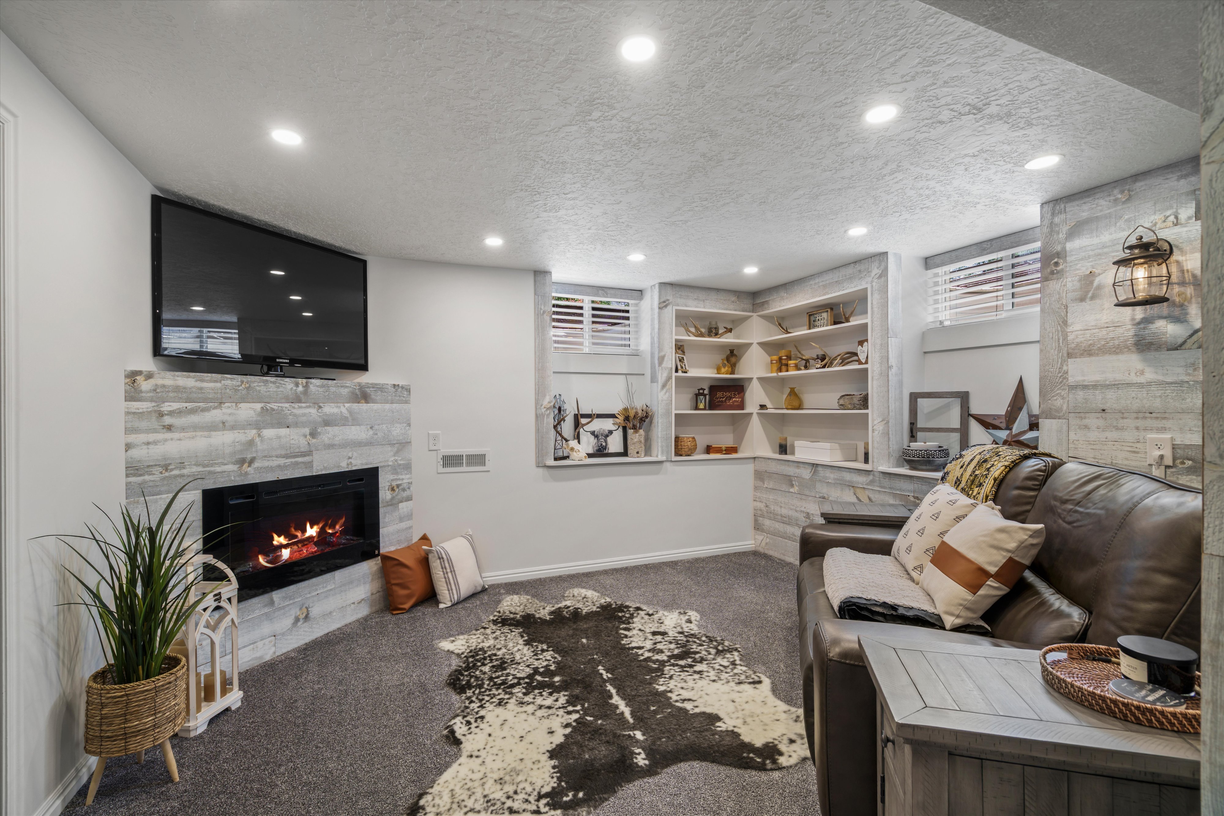 Recessed lighting illuminates a carpeted room featuring a fireplace with a light-toned stacked stone surround. Flexible use space, currently large primary bedroom.