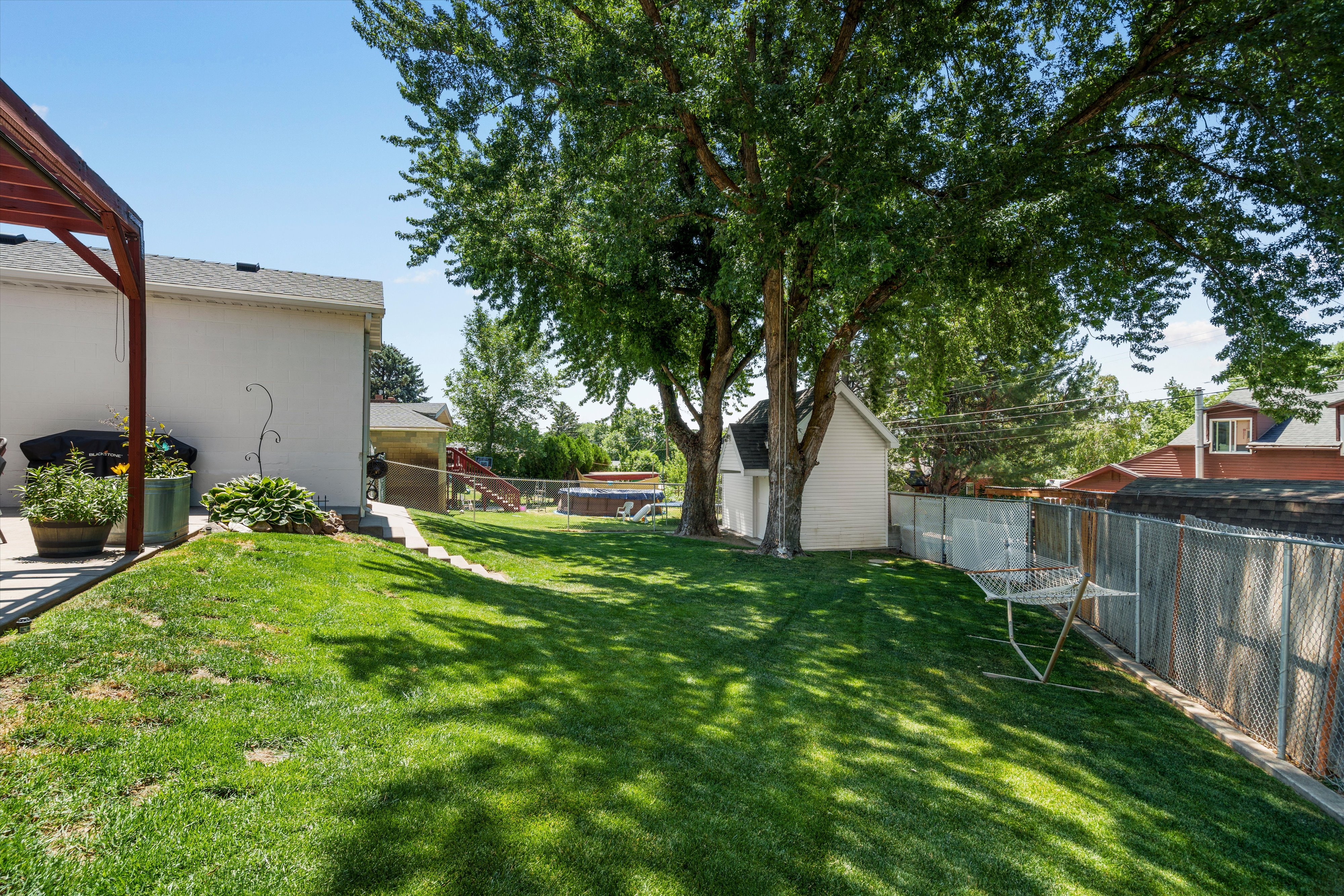 Expansive backyard featuring a manicured lawn, mature trees providing natural shade, a white shed, and full perimeter fencing