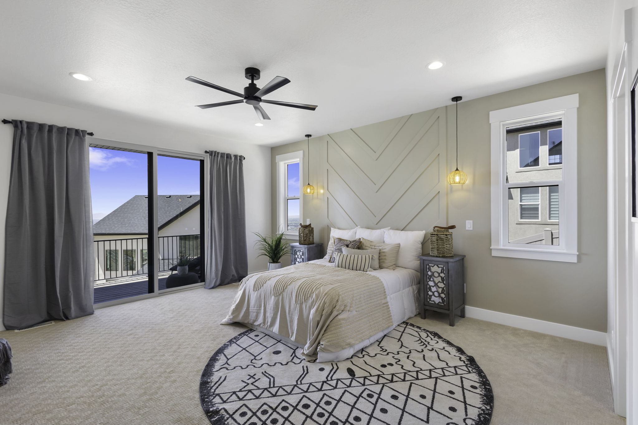 Carpeted bedroom featuring a sliding glass door to a private balcony with black metal railing, a wall-mounted herringbone accent panel, a window with white trim, and a black ceiling fan with integrated lighting