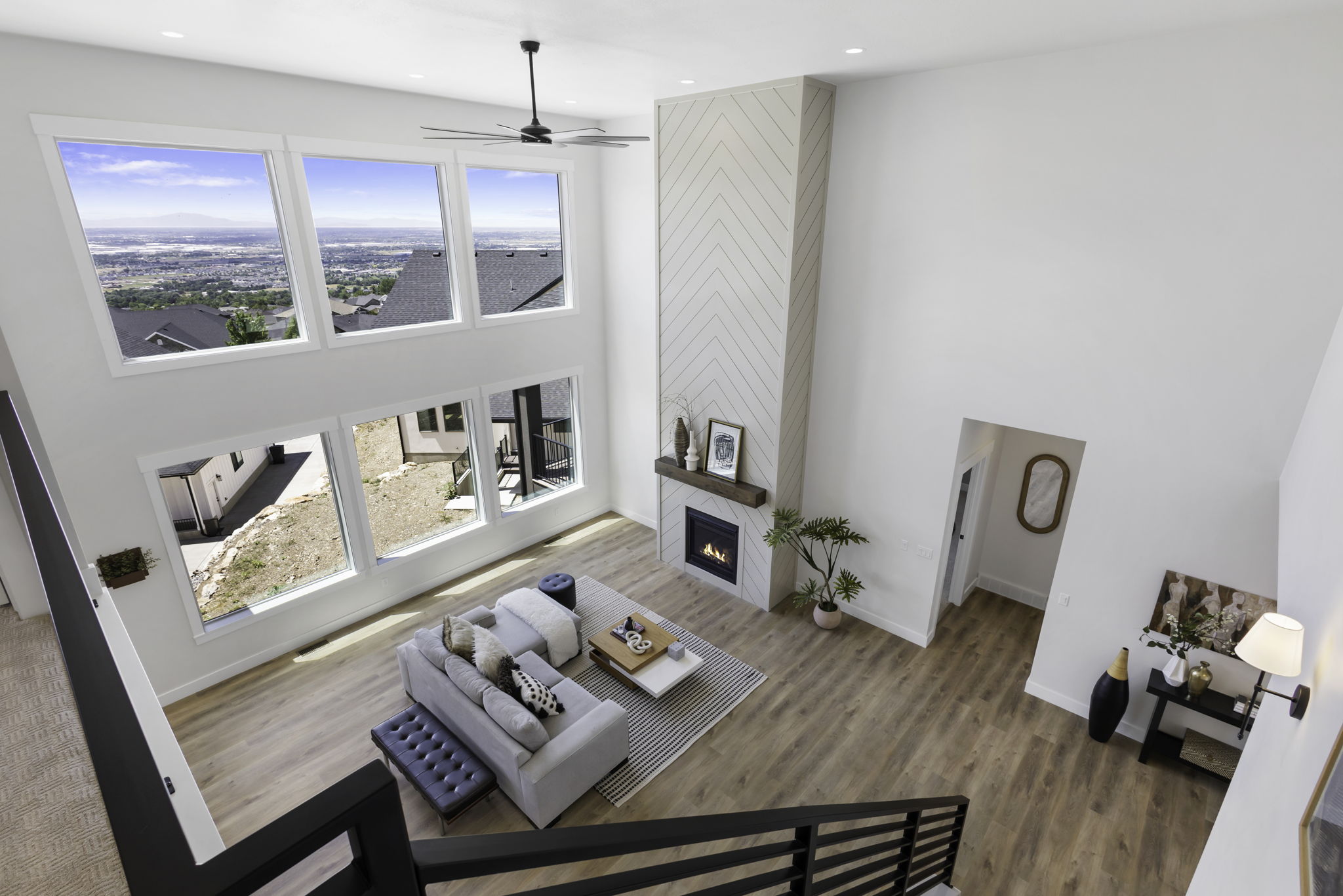 Two-story living area featuring six large windows, a chevron-patterned fireplace surround with a wood mantel, wood-finish flooring, a contemporary ceiling fan, and recessed lighting