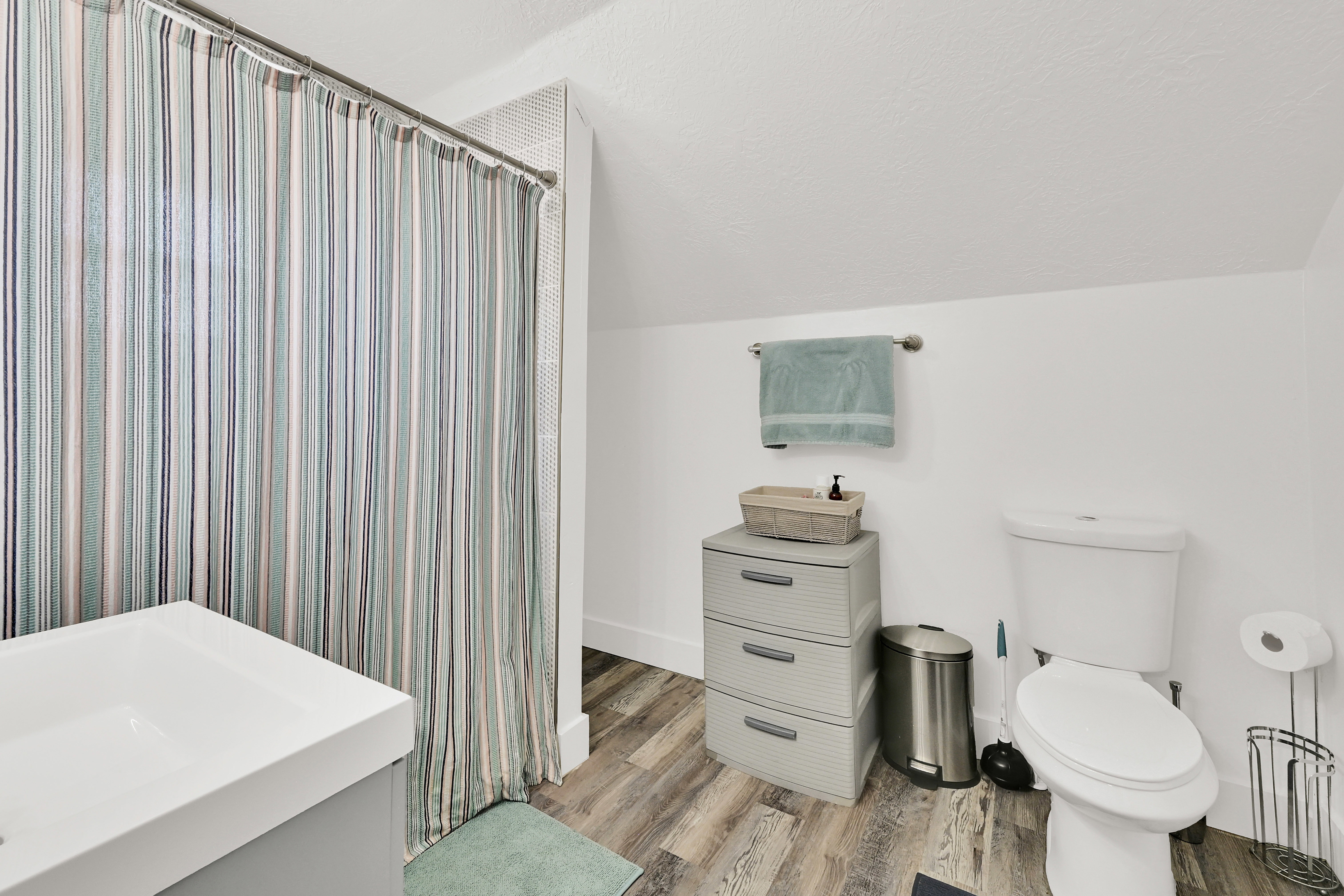 Bathroom featuring a white toilet, contemporary vanity with white basin, and wood-finish flooring