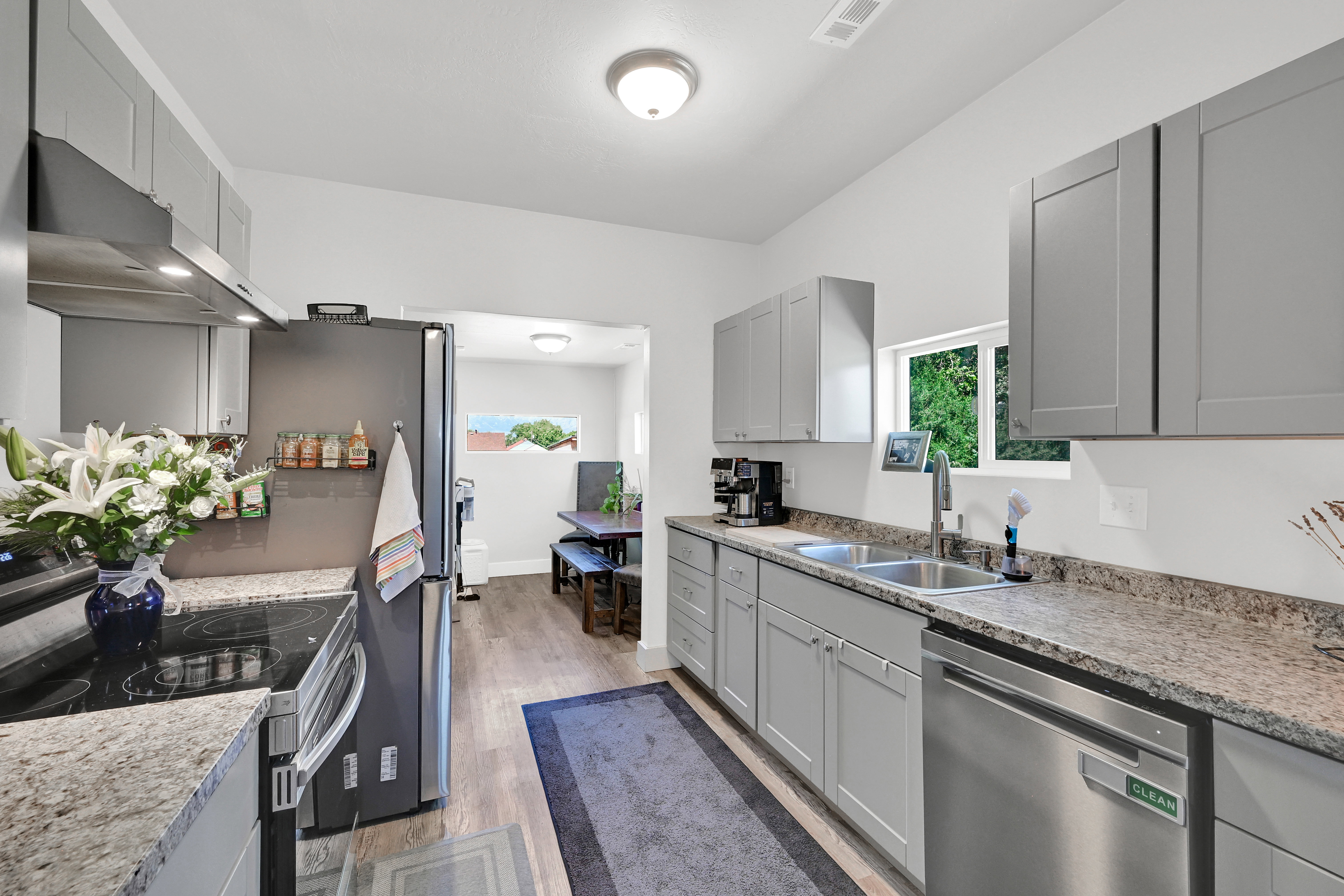 Kitchen featuring light gray cabinetry, stainless steel appliances, speckled countertops, wood-finish flooring, and a double basin sink