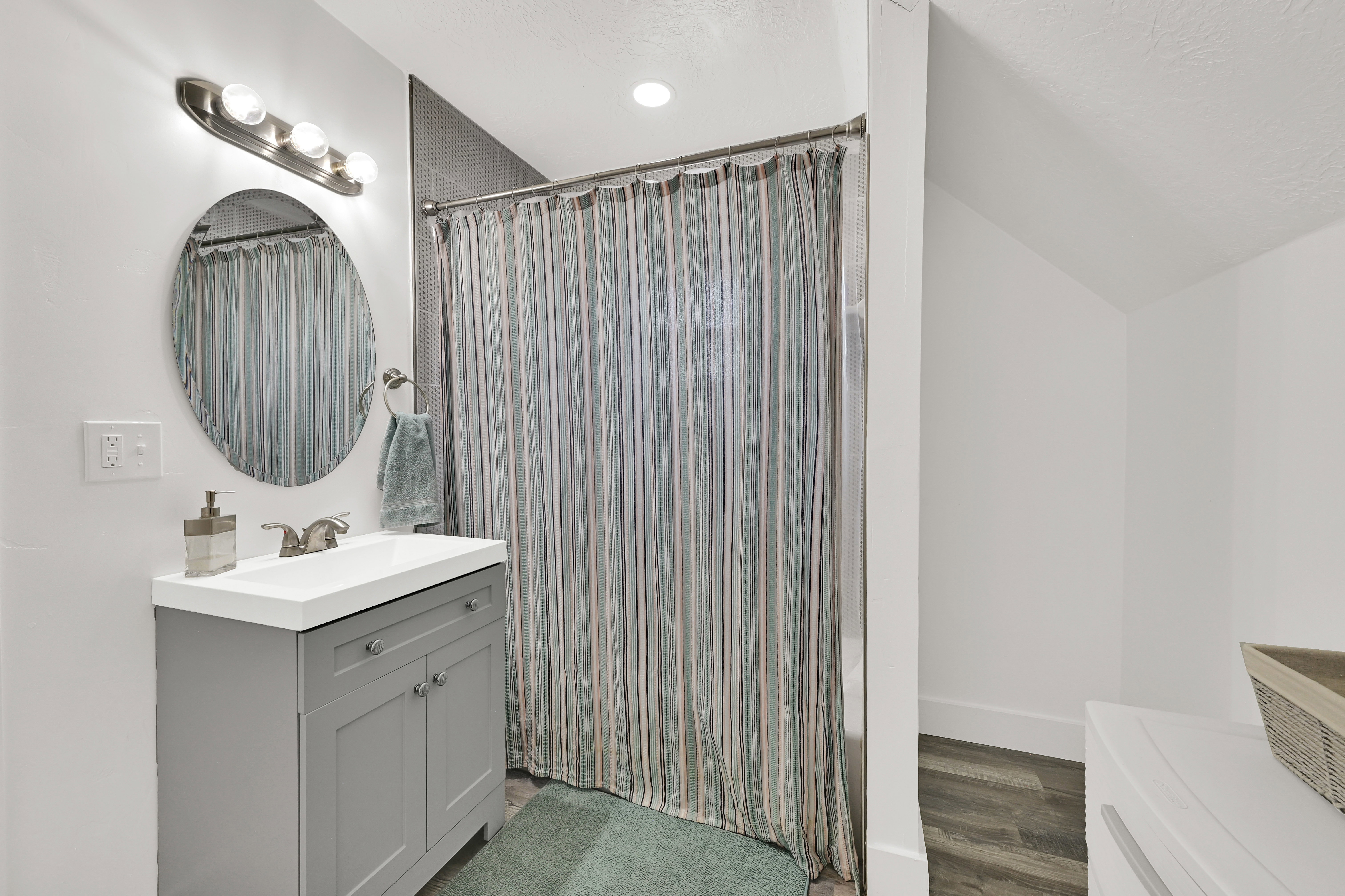 Bathroom featuring a gray vanity with an integrated white sink, an oval mirror, and brushed nickel fixtures