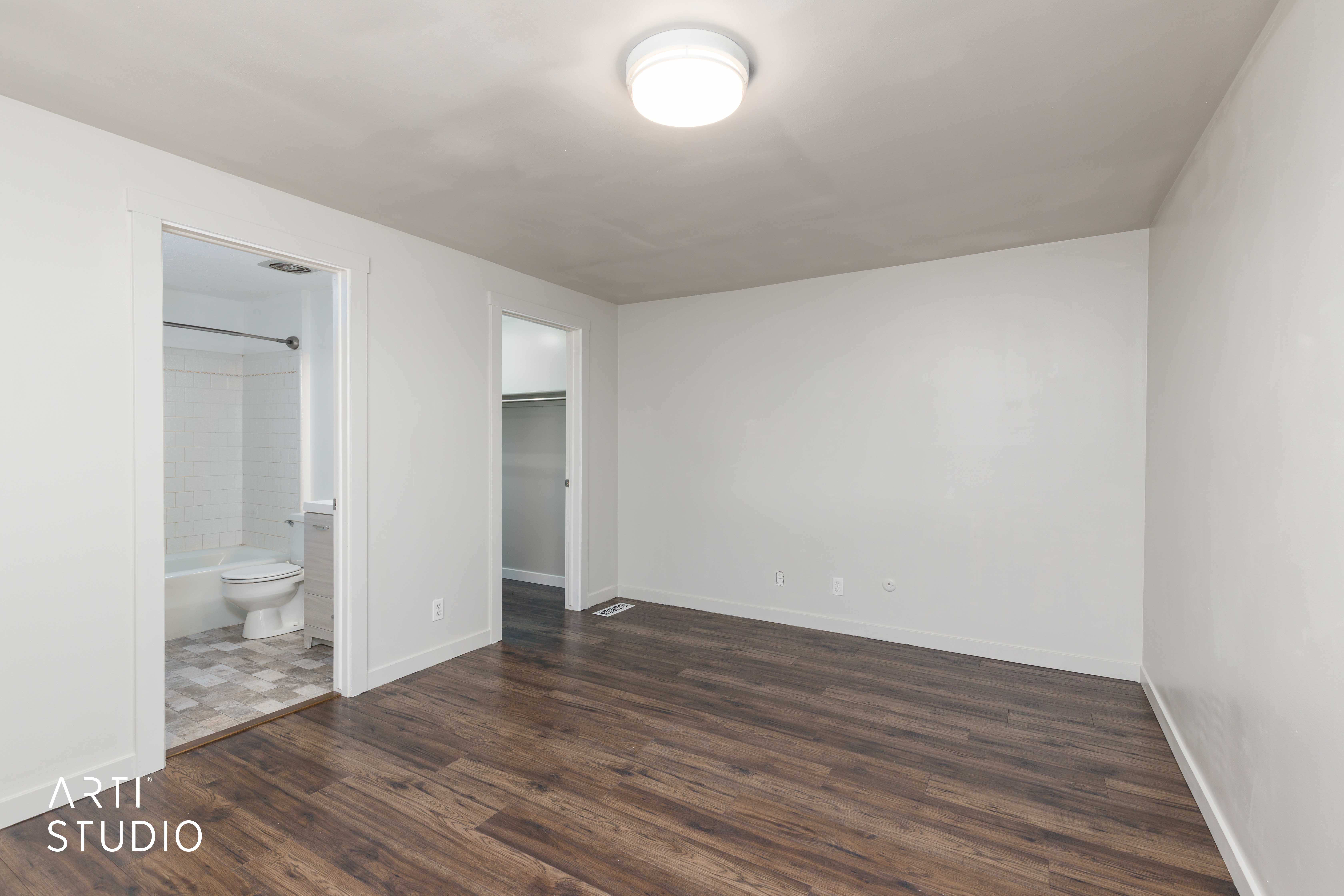 Spacious room featuring dark wood-finish flooring and white painted walls