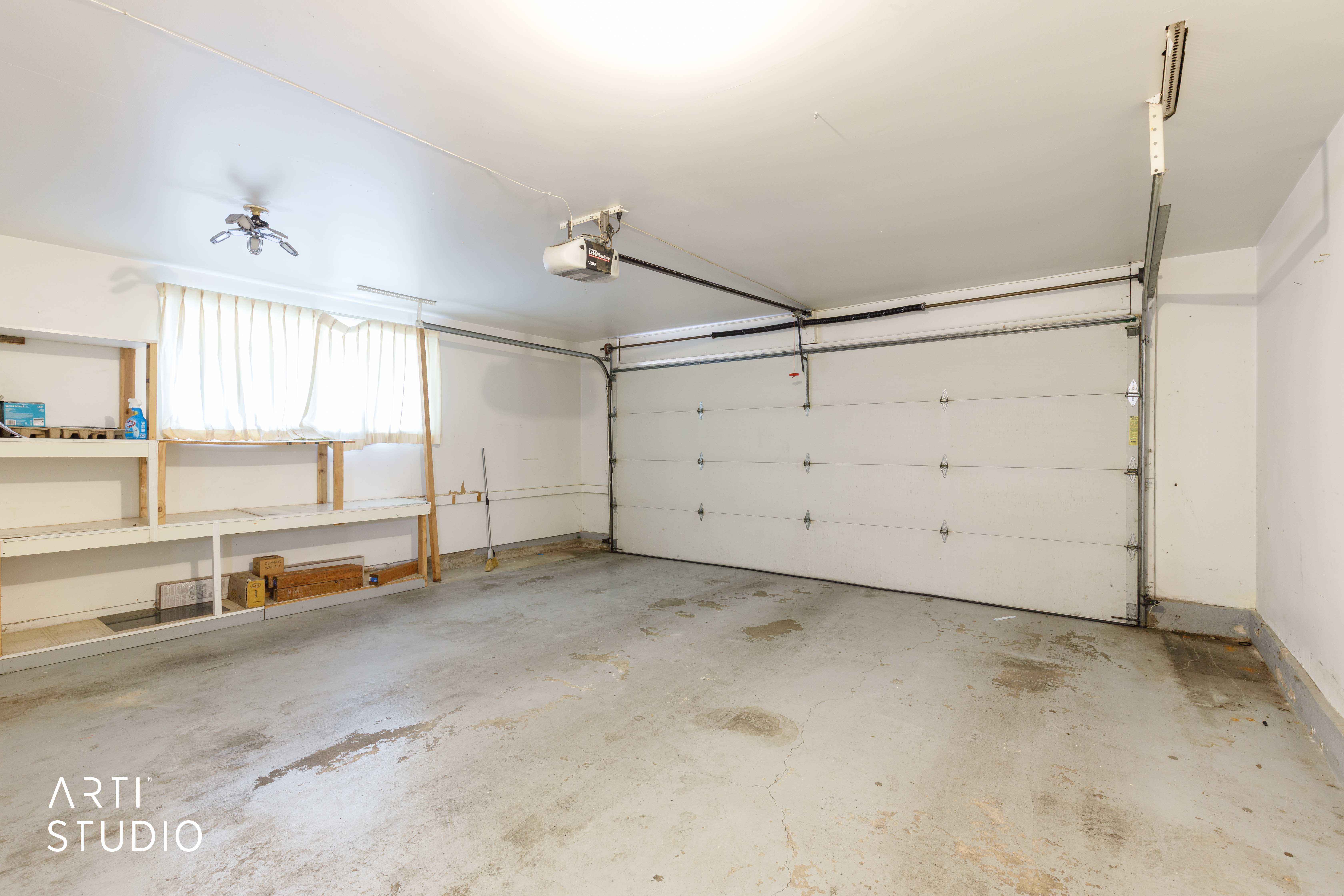 Spacious garage featuring a sectional overhead door, built-in shelving, a window with curtains, an overhead light fixture, and an automatic garage door opener