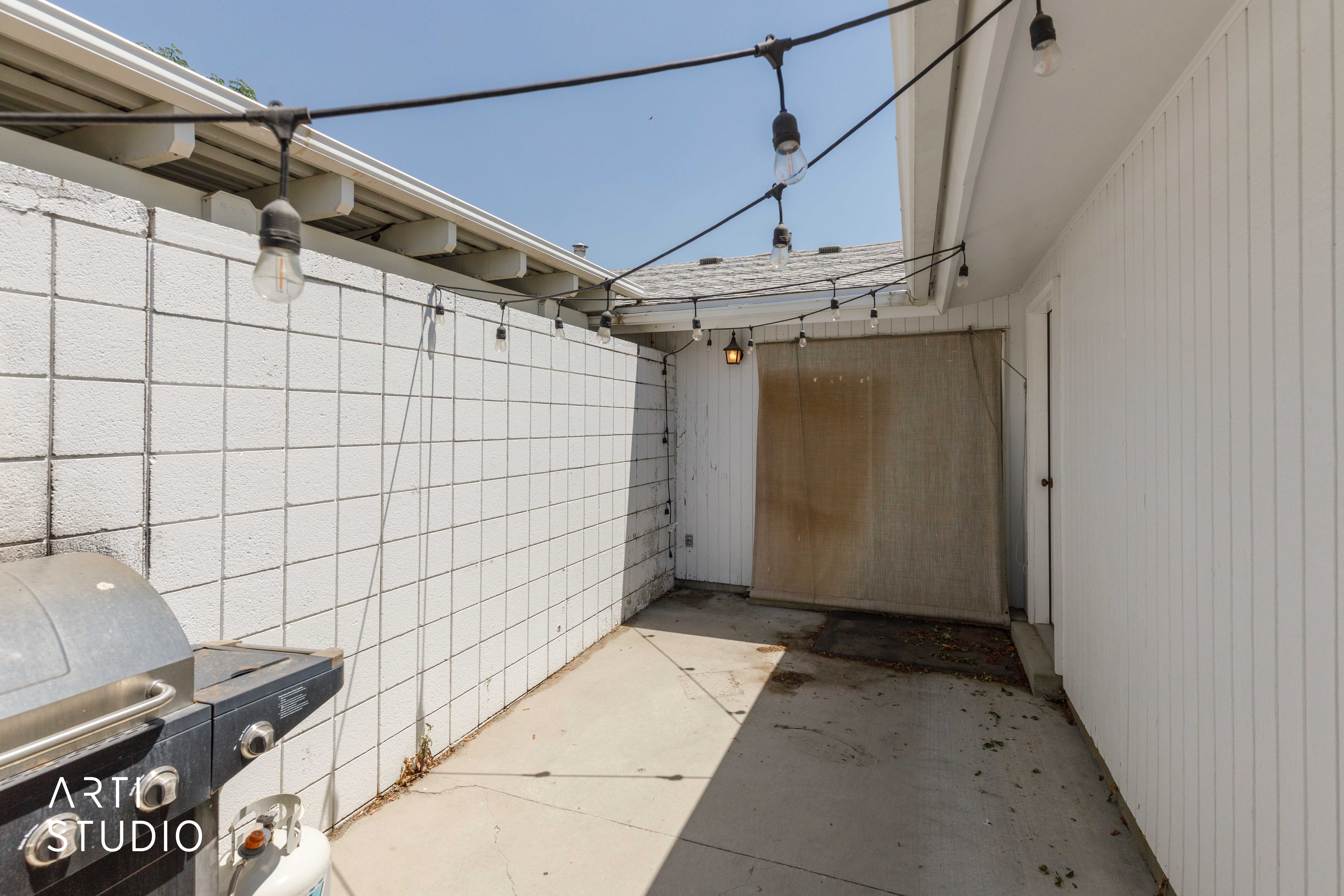 Concrete patio area featuring string lighting, white stucco block wall, and white vertical siding