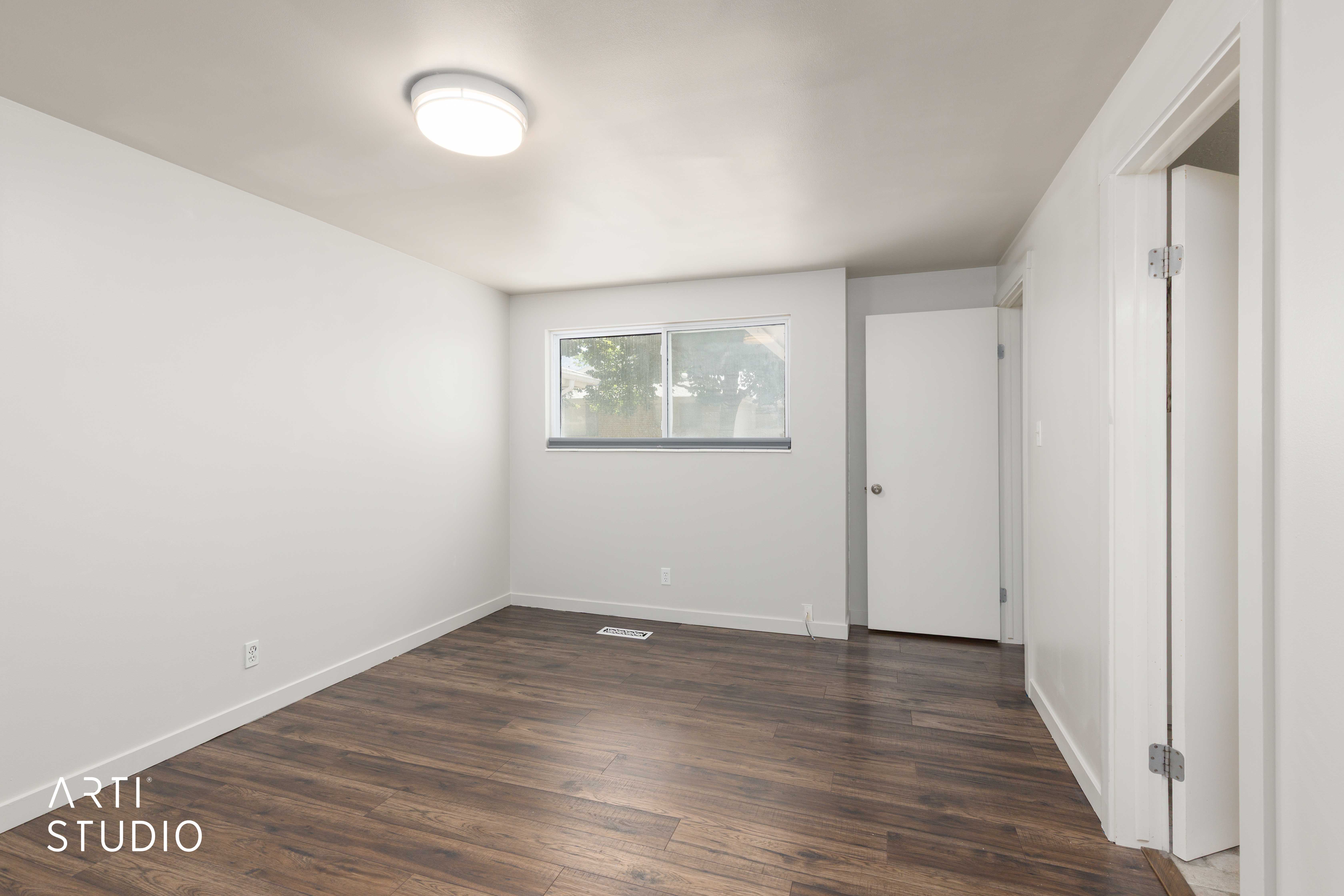 Room featuring wood-finish flooring, white baseboards, a window with exterior views, and a flush-mount ceiling light