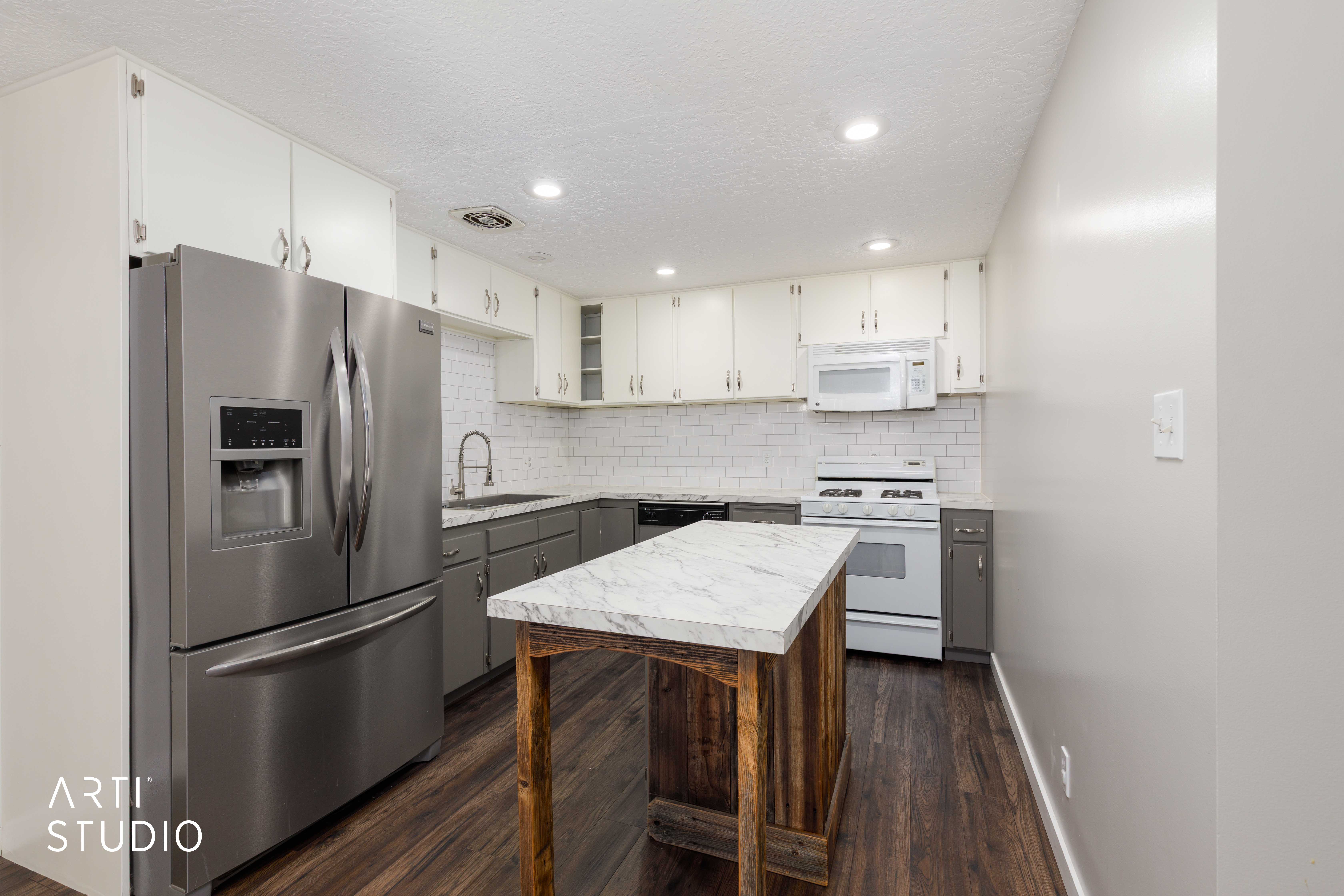 Updated kitchen featuring wood-finish flooring, white subway tile backsplash, recessed lighting, and a stainless steel refrigerator