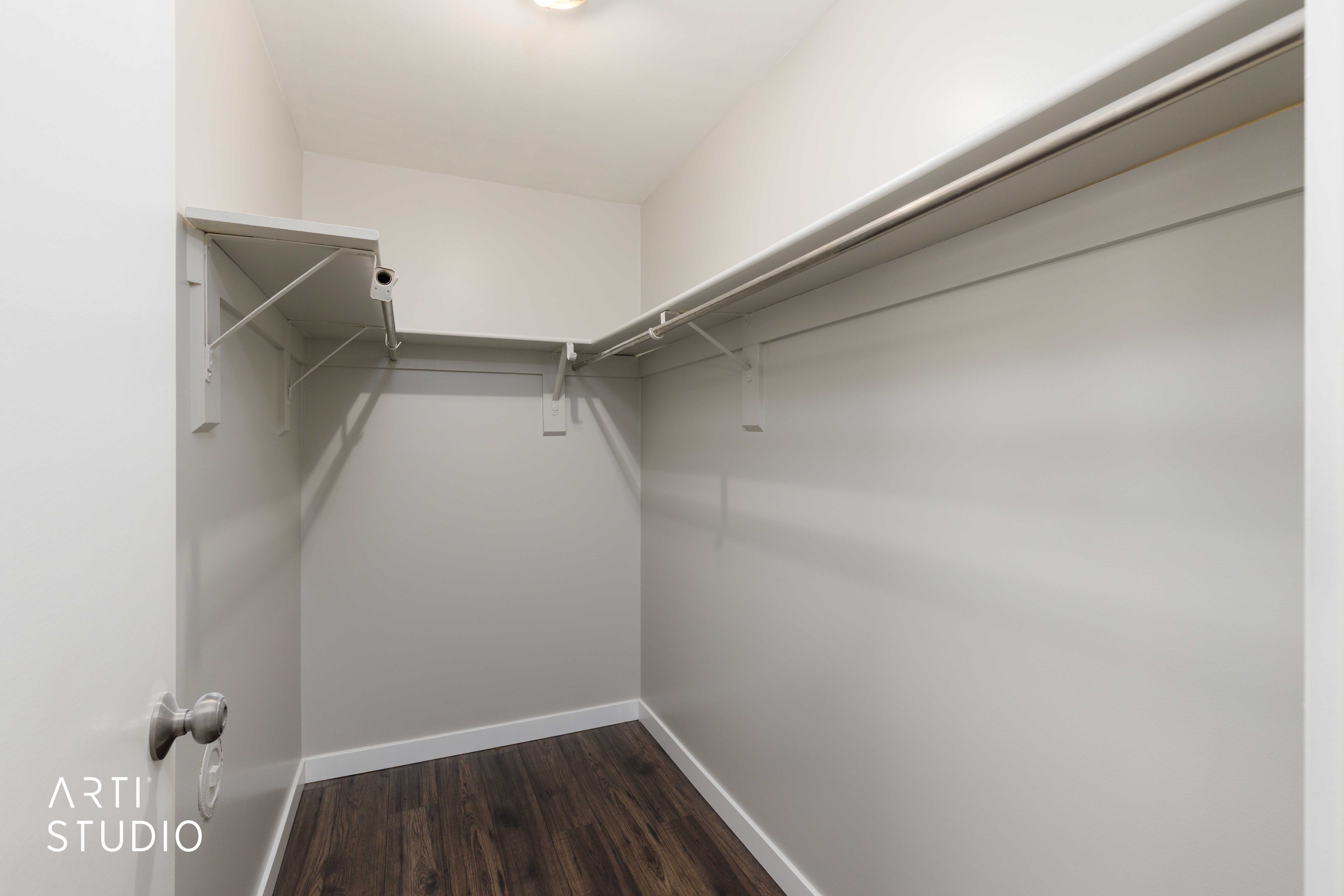 Walk-in closet featuring wood-finish flooring, white baseboards, a built-in overhead light, and a shelving system with multiple hanging rods