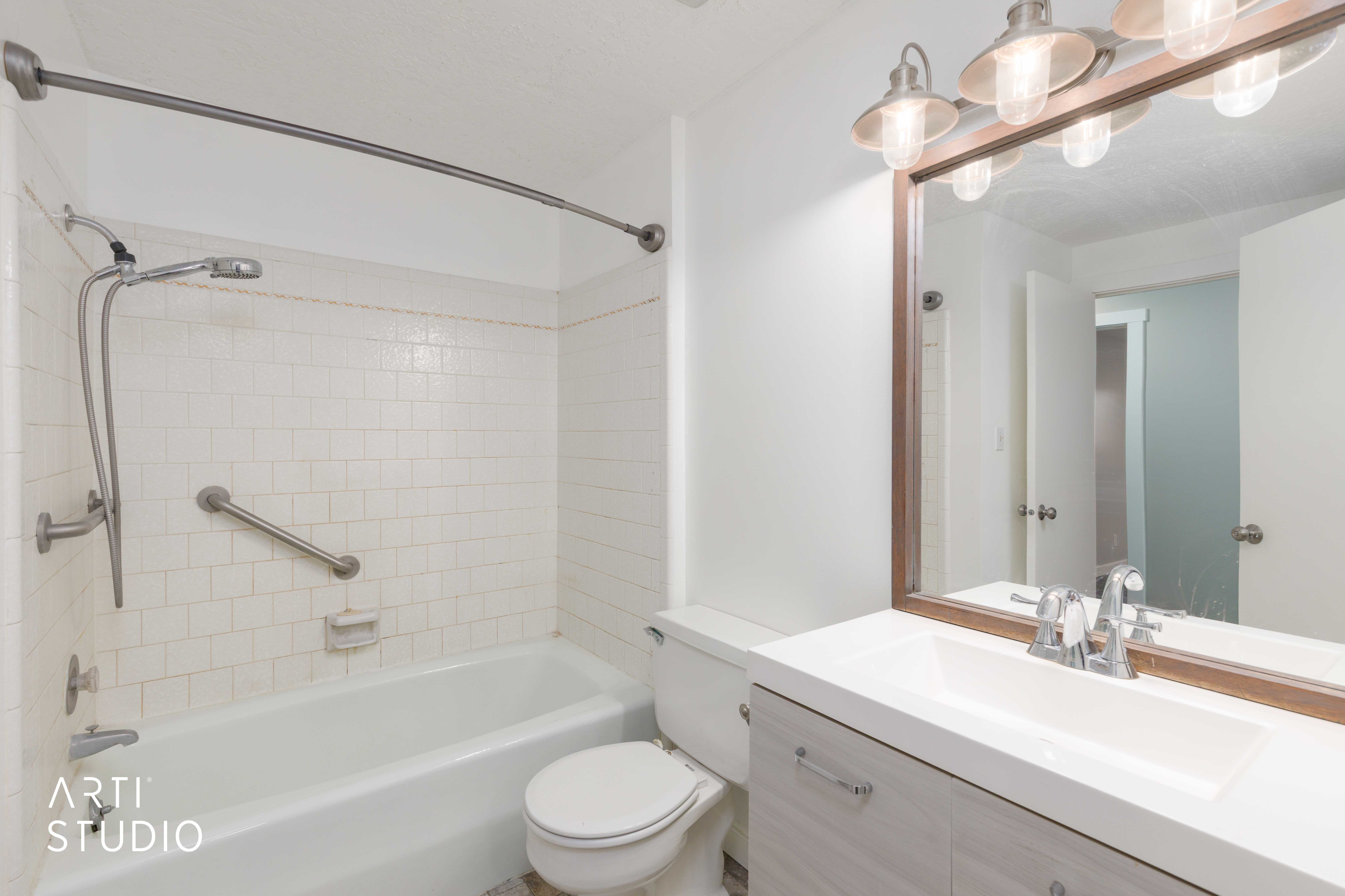 Bathroom featuring a tub/shower combination with white subway tile surround, chrome fixtures, a wood-framed mirror, a vanity with an integrated sink, and a multi-bulb light fixture