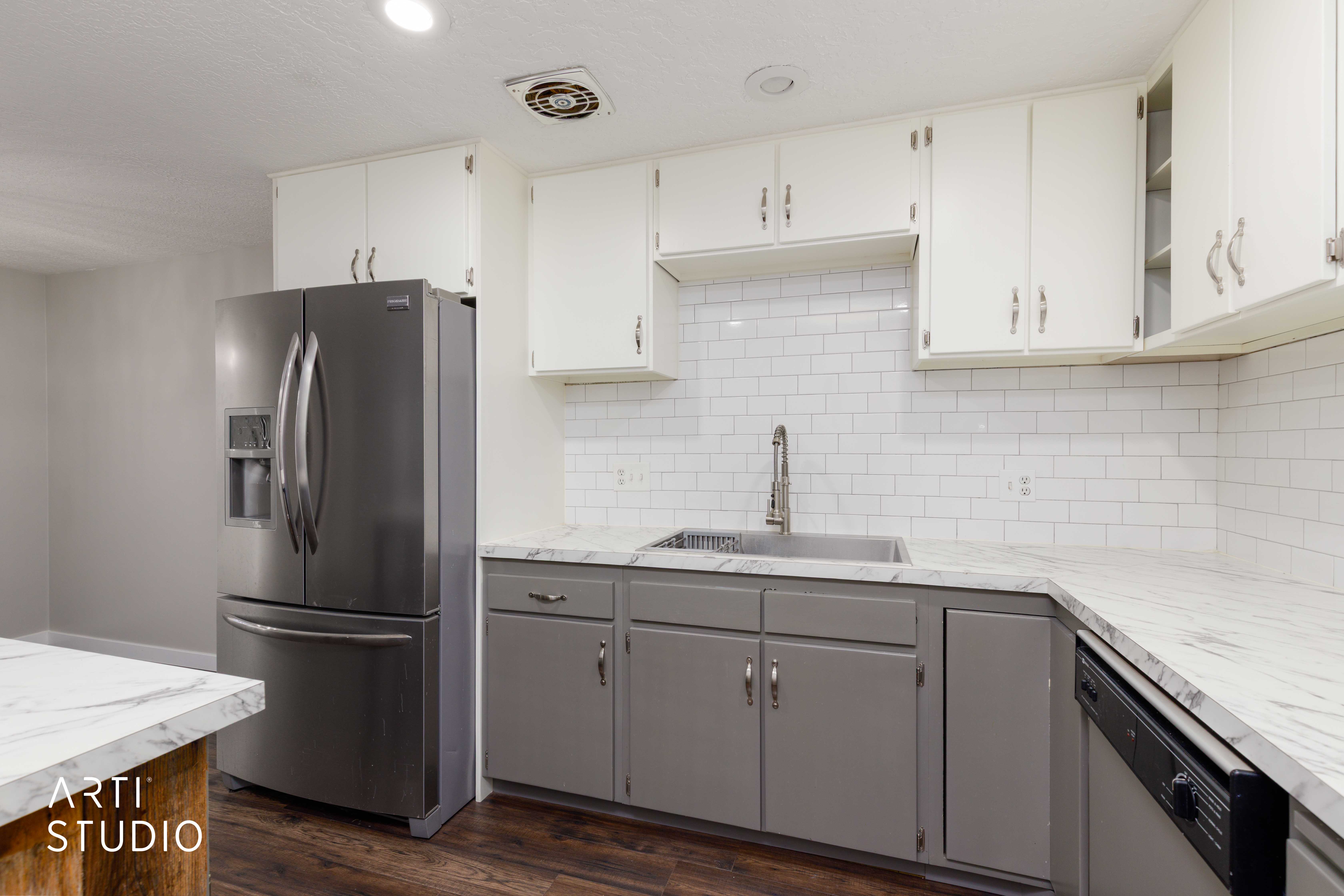 Kitchen featuring white subway tile backsplash, white upper cabinetry, gray lower cabinetry, and light-toned countertops
