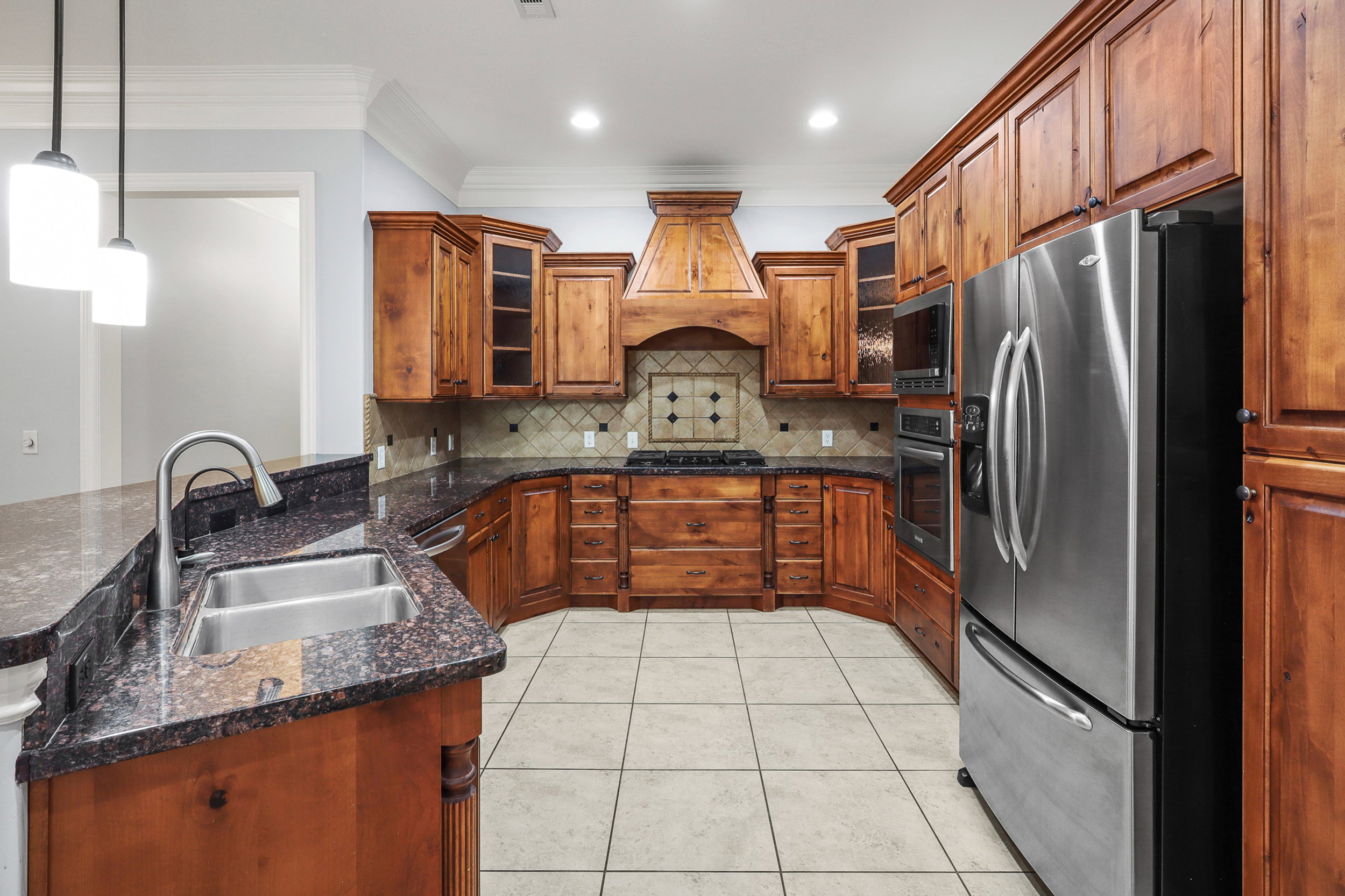Kitchen featuring wood cabinetry, granite countertops, tile flooring, stainless steel appliances, and a tile backsplash