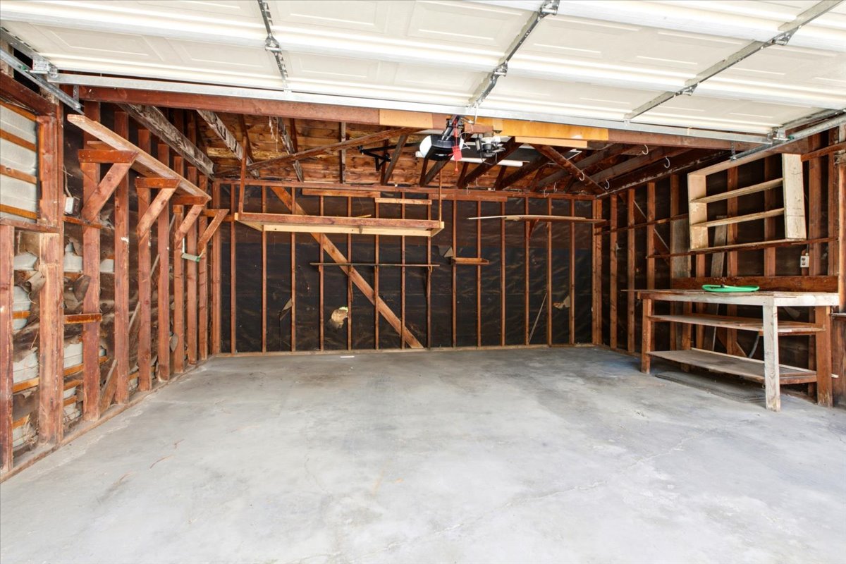 Garage interior featuring exposed wood framing, concrete flooring, overhead garage door, built-in workbench, and built-in shelving
