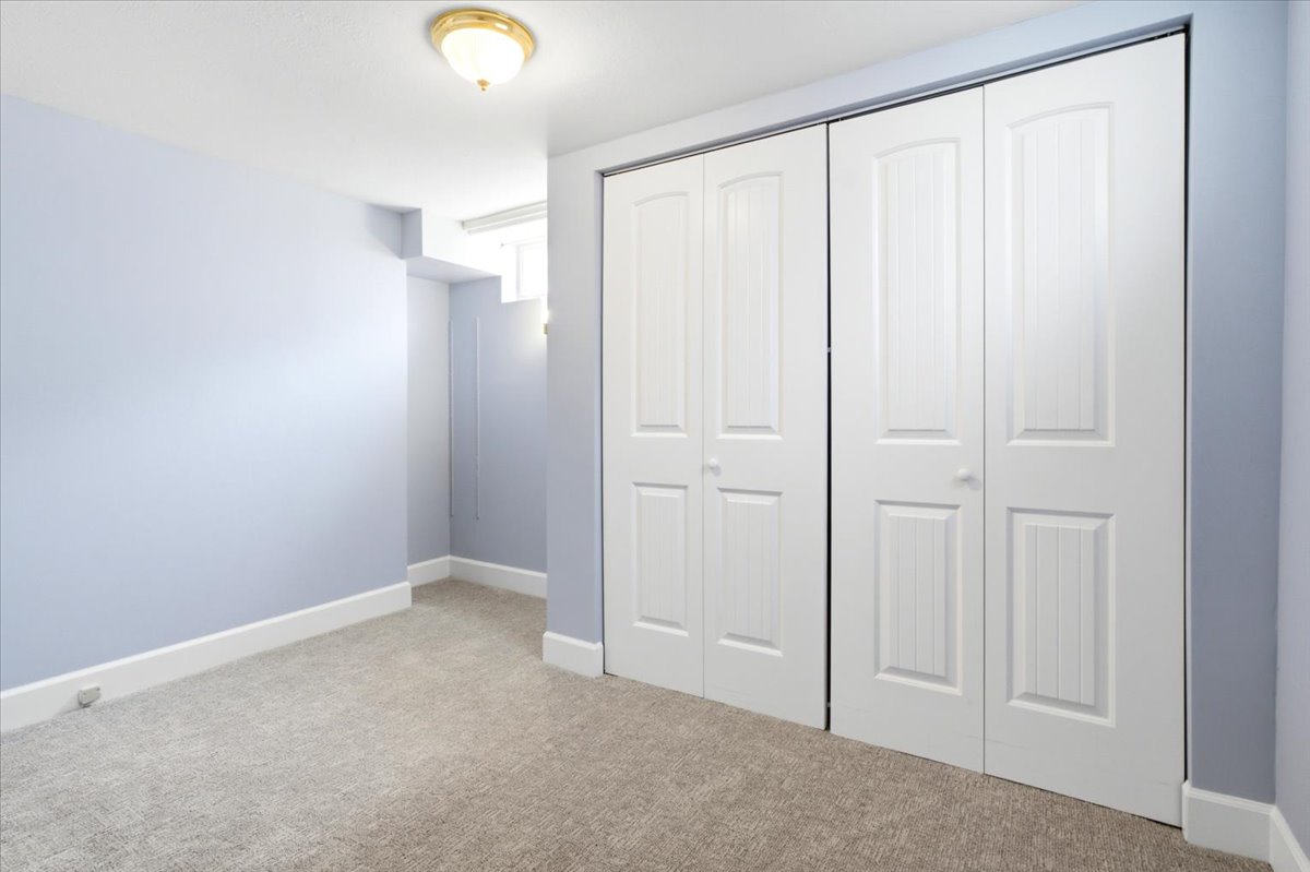 Spacious interior featuring a large closet with paneled bifold doors, light blue wall paint, white baseboards, and neutral-toned carpeting