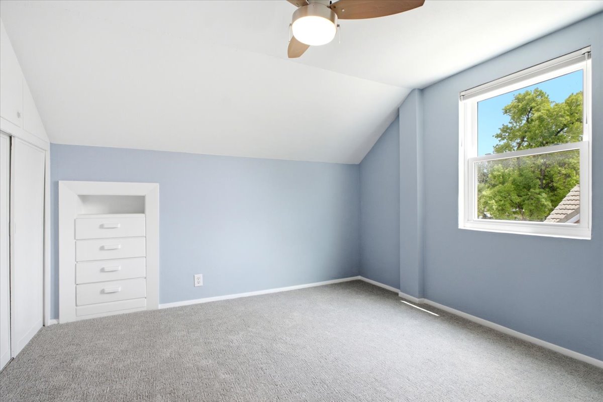 Carpeted room featuring an angled ceiling, a ceiling fan with light, a window with white trim, and a built-in dresser with four drawers