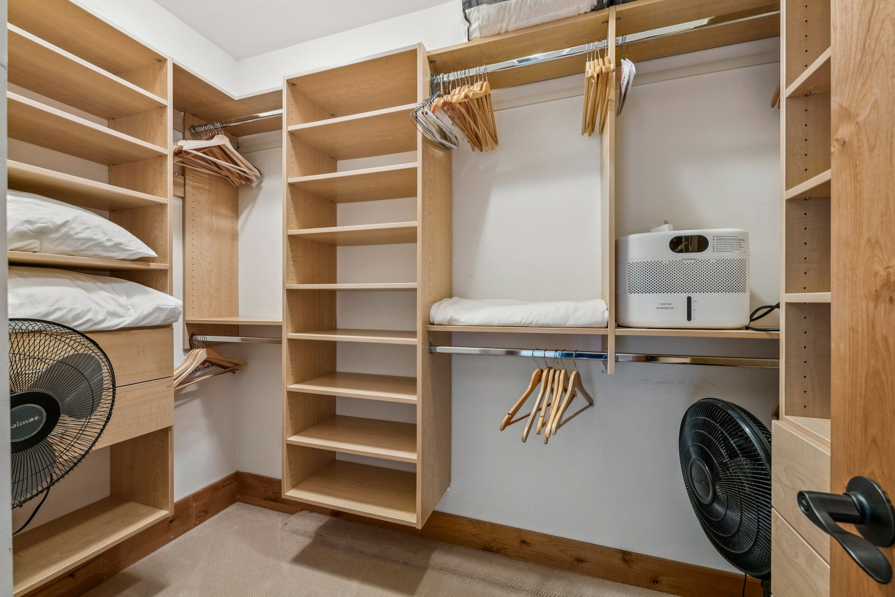 Custom closet system featuring light wood-finish shelving, multiple hanging rods, built-in drawers, and extensive storage compartments