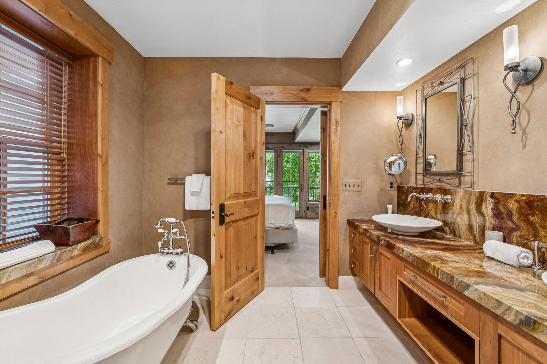Bathroom featuring a clawfoot soaking tub, wood-finish window blinds, a spacious wood vanity with a vessel sink, and a multi-toned stone countertop