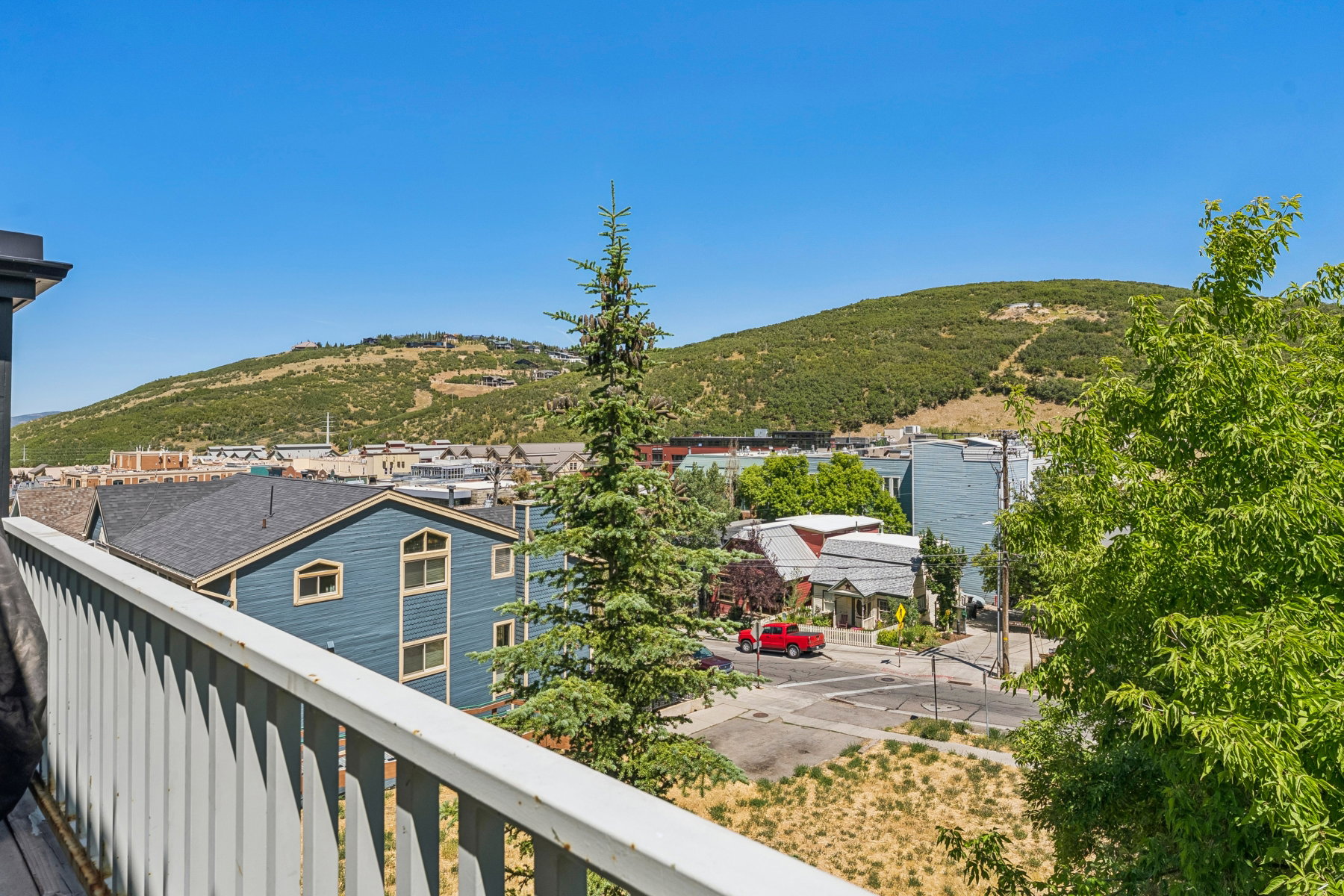 Balcony with white vertical railing overlooking a neighborhood with varied architecture and distant green hills
