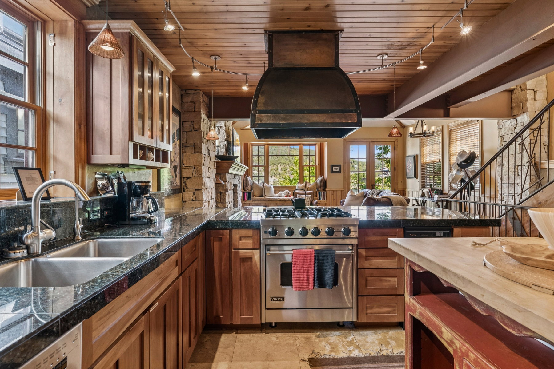 Gourmet kitchen featuring a stainless steel gas range, stone countertops, natural wood cabinetry, and a custom range hood