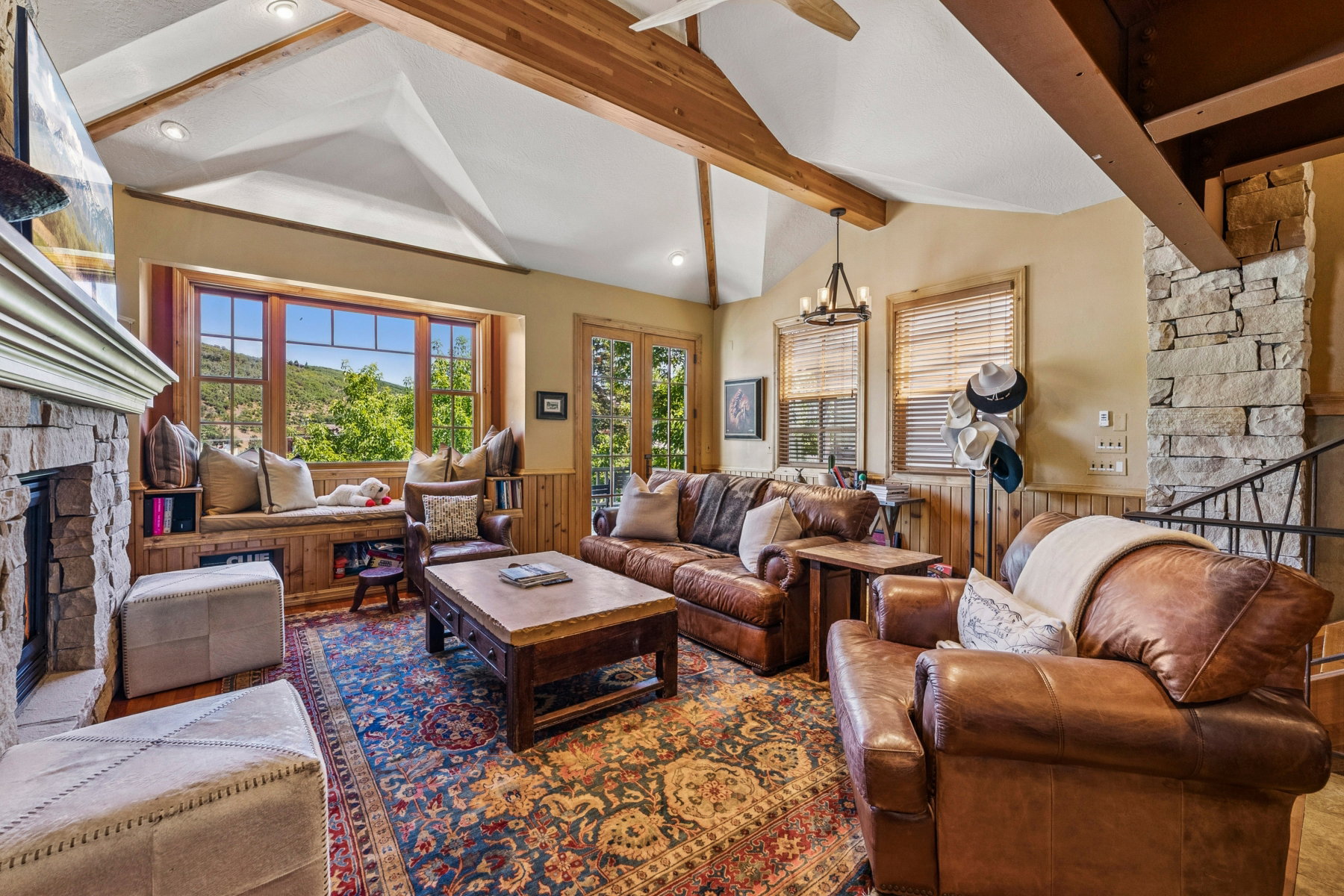 Living area featuring a stone fireplace with a substantial mantel, a built-in window seat with storage, exposed wood ceiling beams, and a chandelier lighting fixture