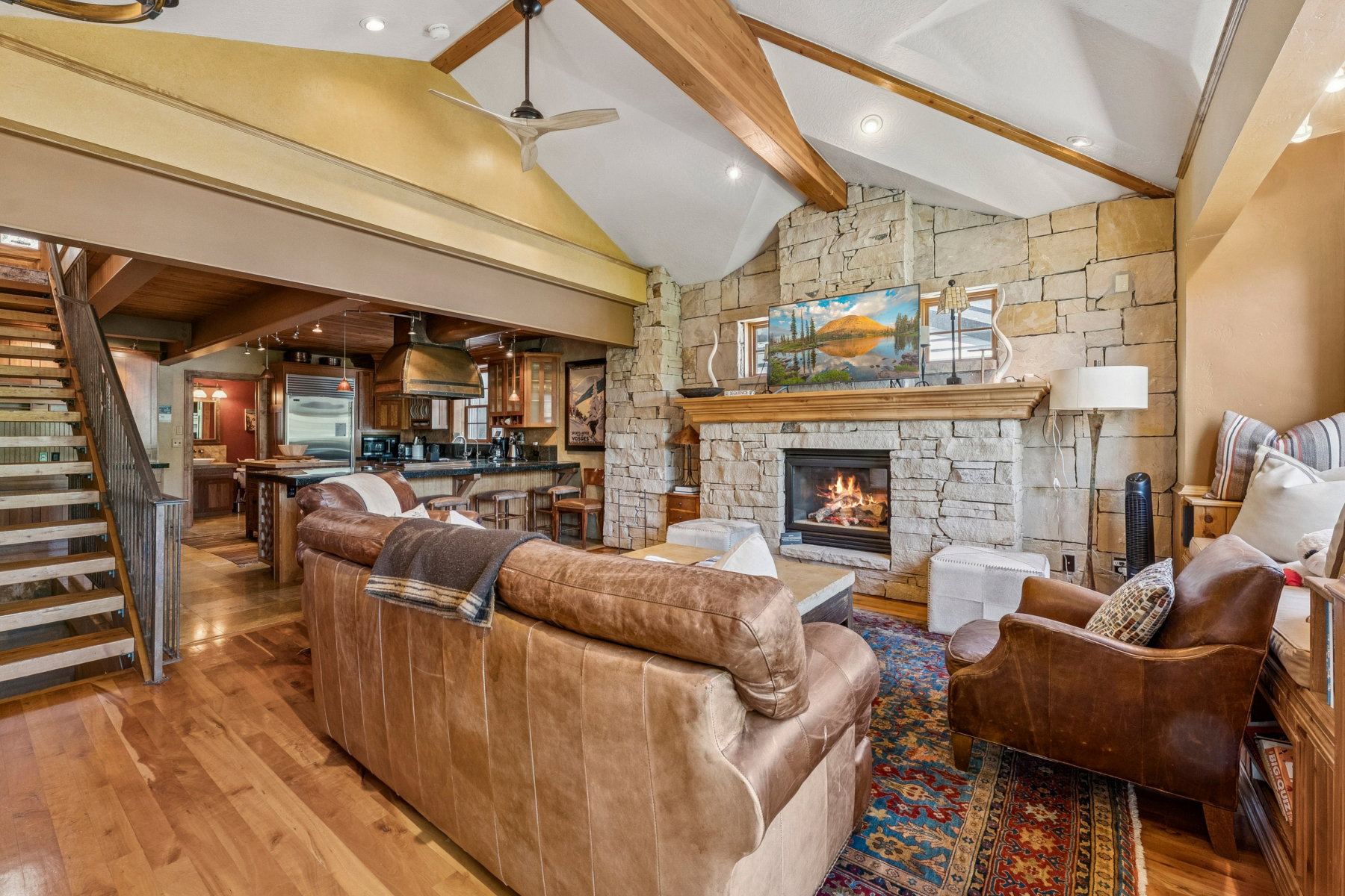 Vaulted ceiling living space featuring a stone fireplace with a wood mantle, exposed wood beams, and wood-finish flooring
