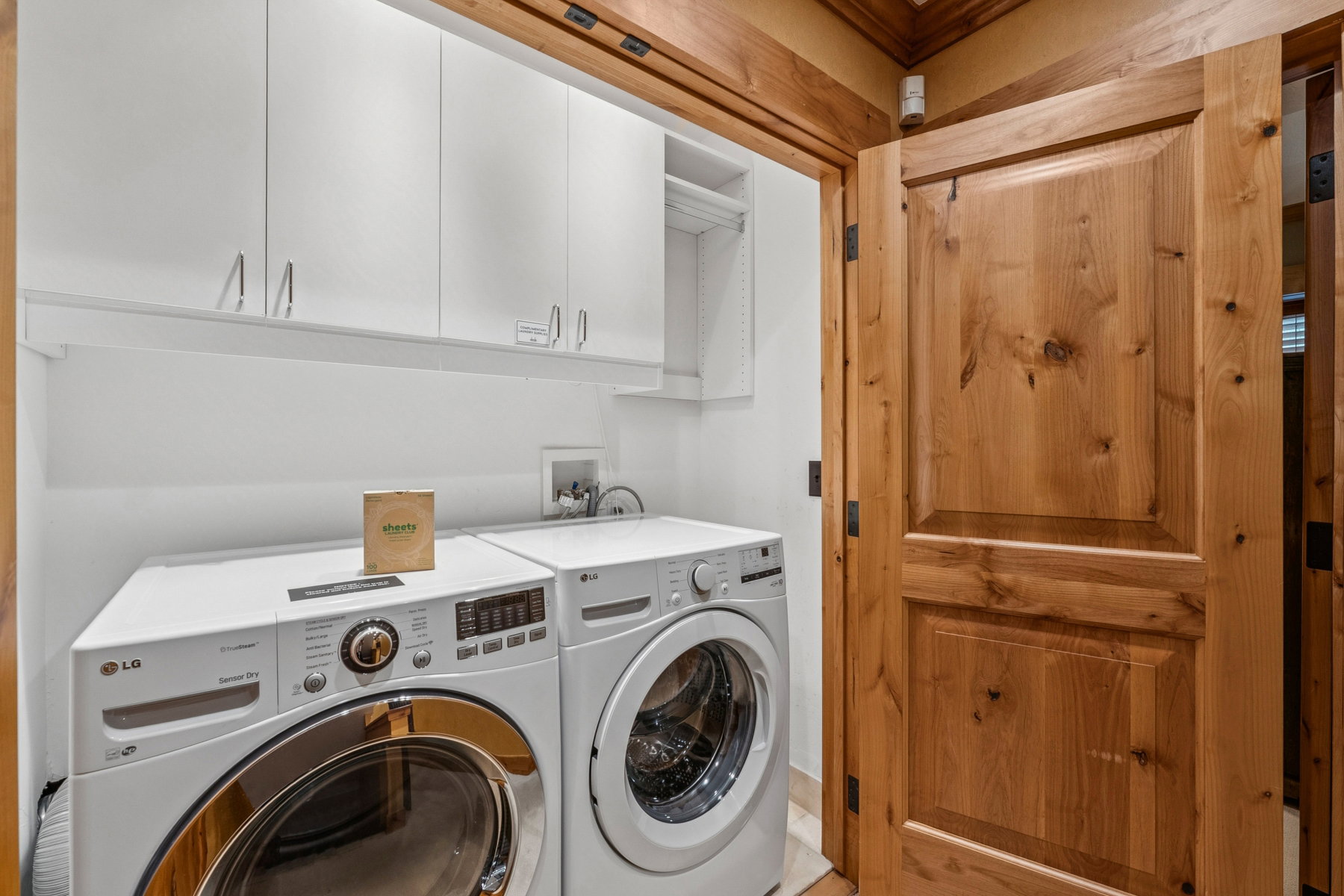 Dedicated laundry area featuring white upper cabinetry, a built-in shelf, and wood paneling on the doorway