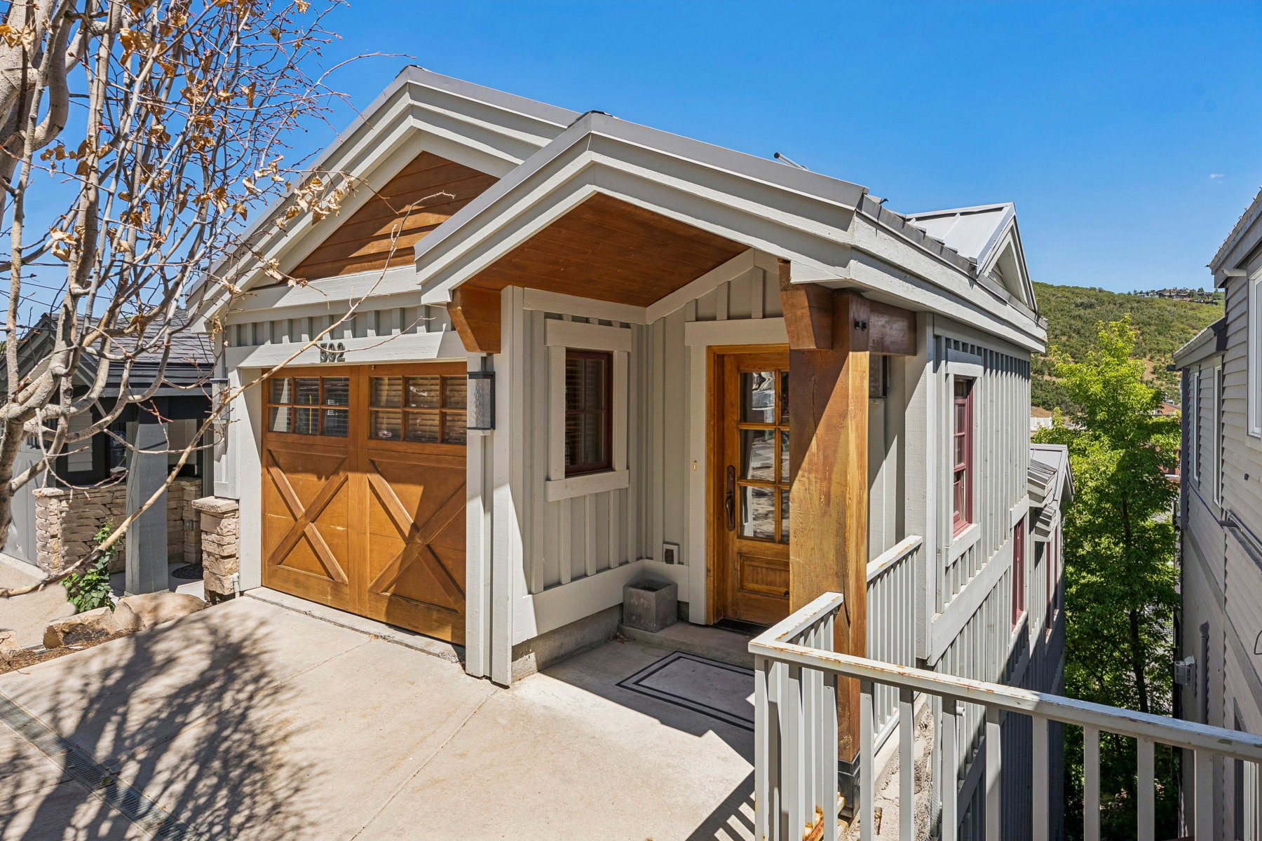 Wood-paneled garage door with transom windows, board and batten siding, substantial wood column, metal roof, and a wood-paneled entry door