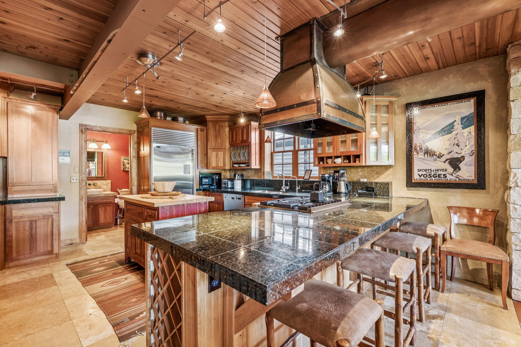 Spacious kitchen featuring a large island with an integrated cooktop, granite countertops, wood-finish cabinetry, and a substantial copper range hood