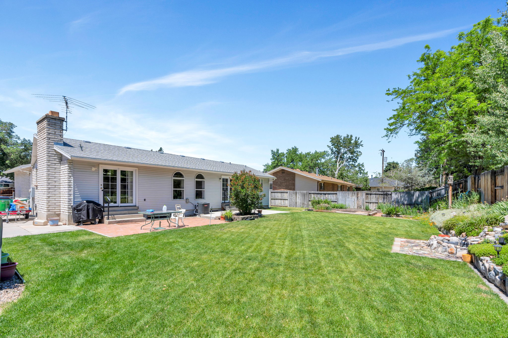 Expansive backyard featuring a large green lawn, a brick paver patio, a decorative rock garden, and mature perimeter trees