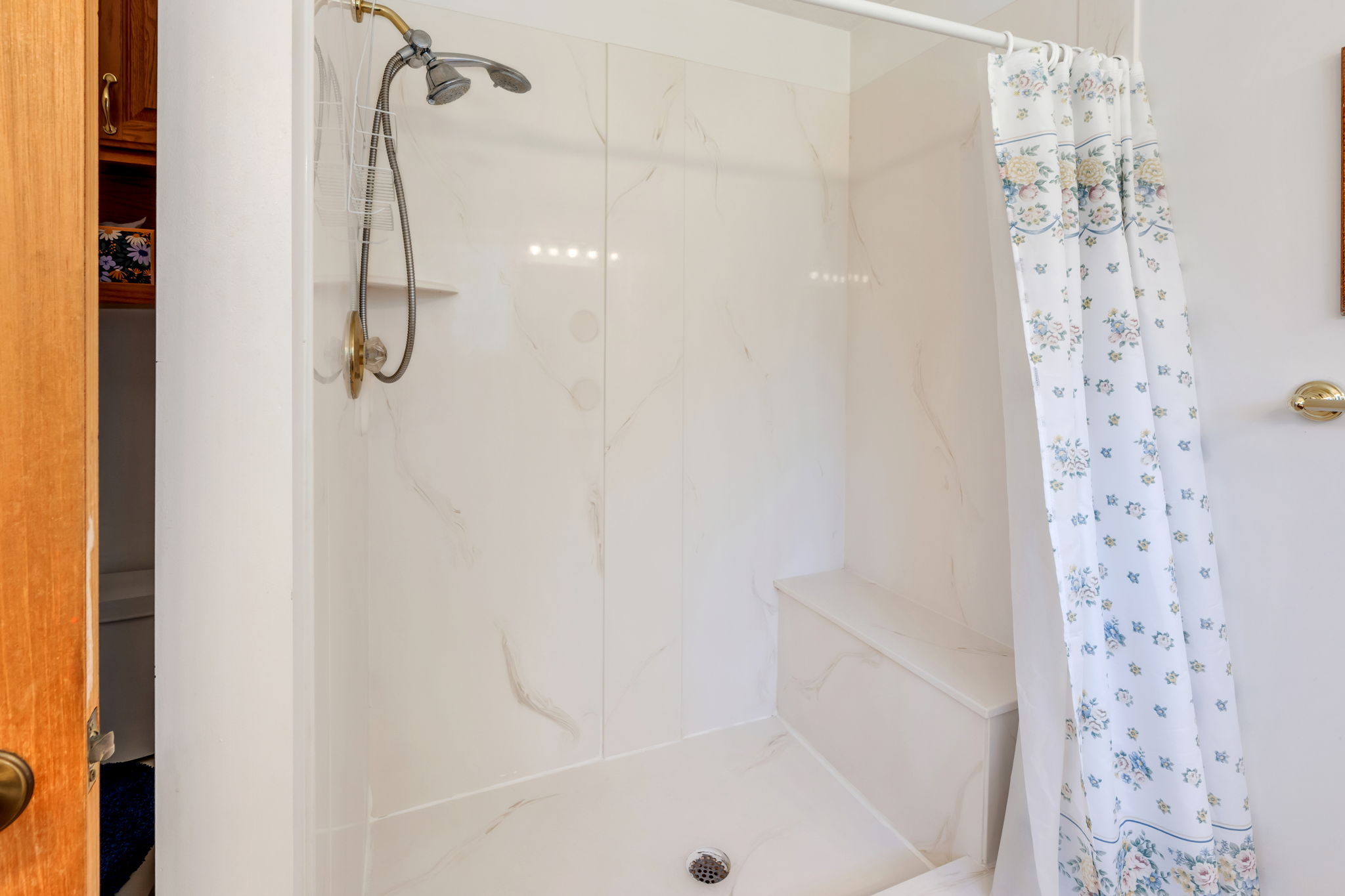 Shower enclosure featuring white paneling with subtle veining, a built-in bench, and a dual-head shower fixture