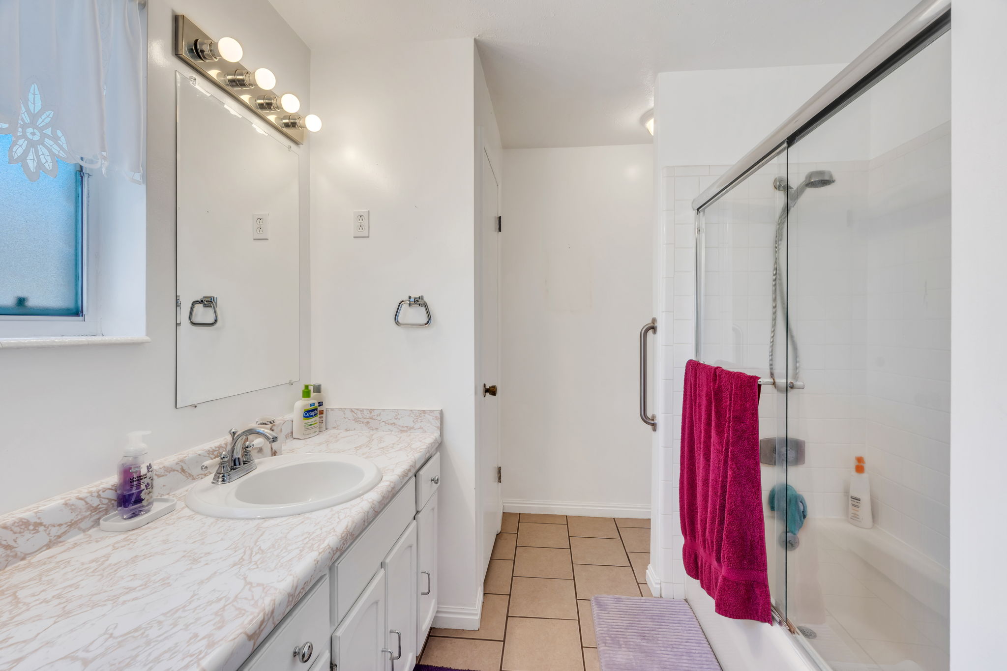 Bathroom featuring a single vanity with a white countertop and undermount sink, a large mirror, a chrome light fixture with five bulbs, and a combination shower/tub with a glass sliding door