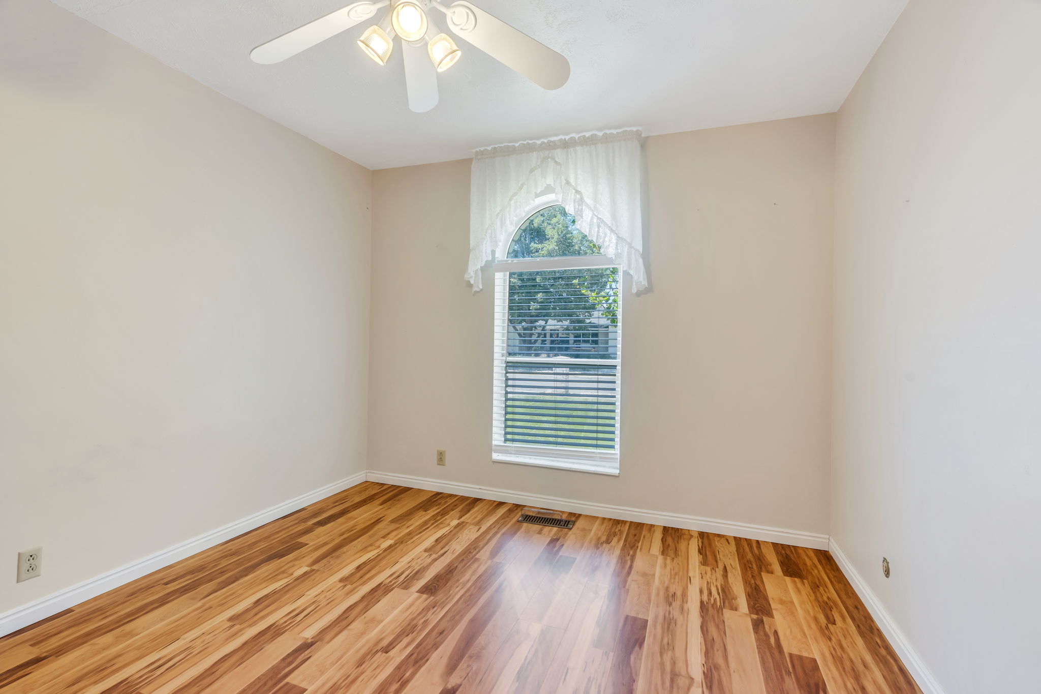 Room featuring wood-finish flooring, a white ceiling fan with integrated lighting, and an arched window with horizontal blinds