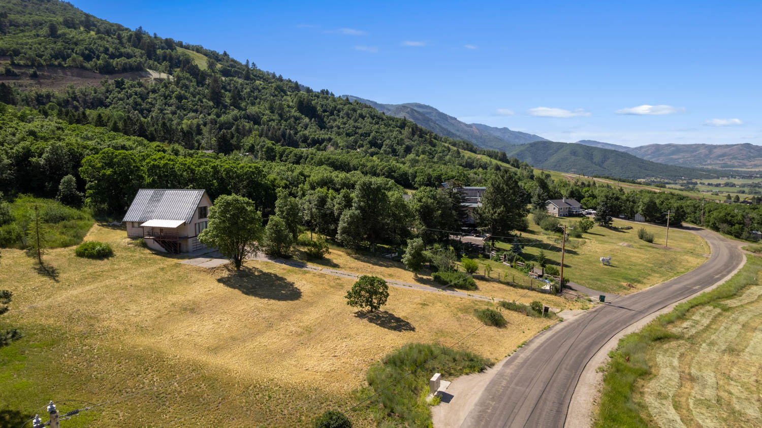 Hillside property featuring a sloped lot, a paved road, and distant mountain ranges