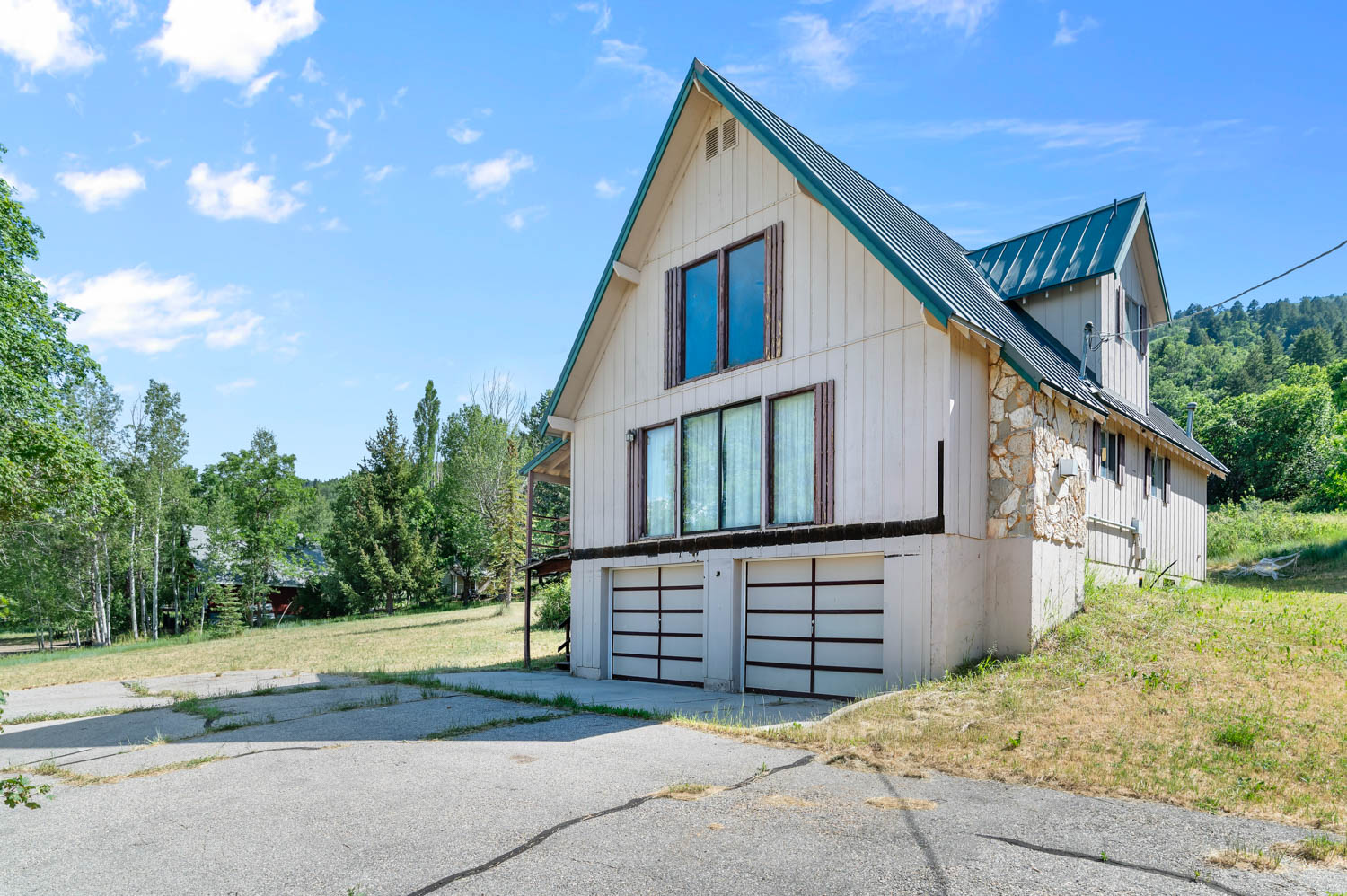 Gable-style home with a metal roof, vertical siding, stone accents, two-car garage, and multiple large windows
