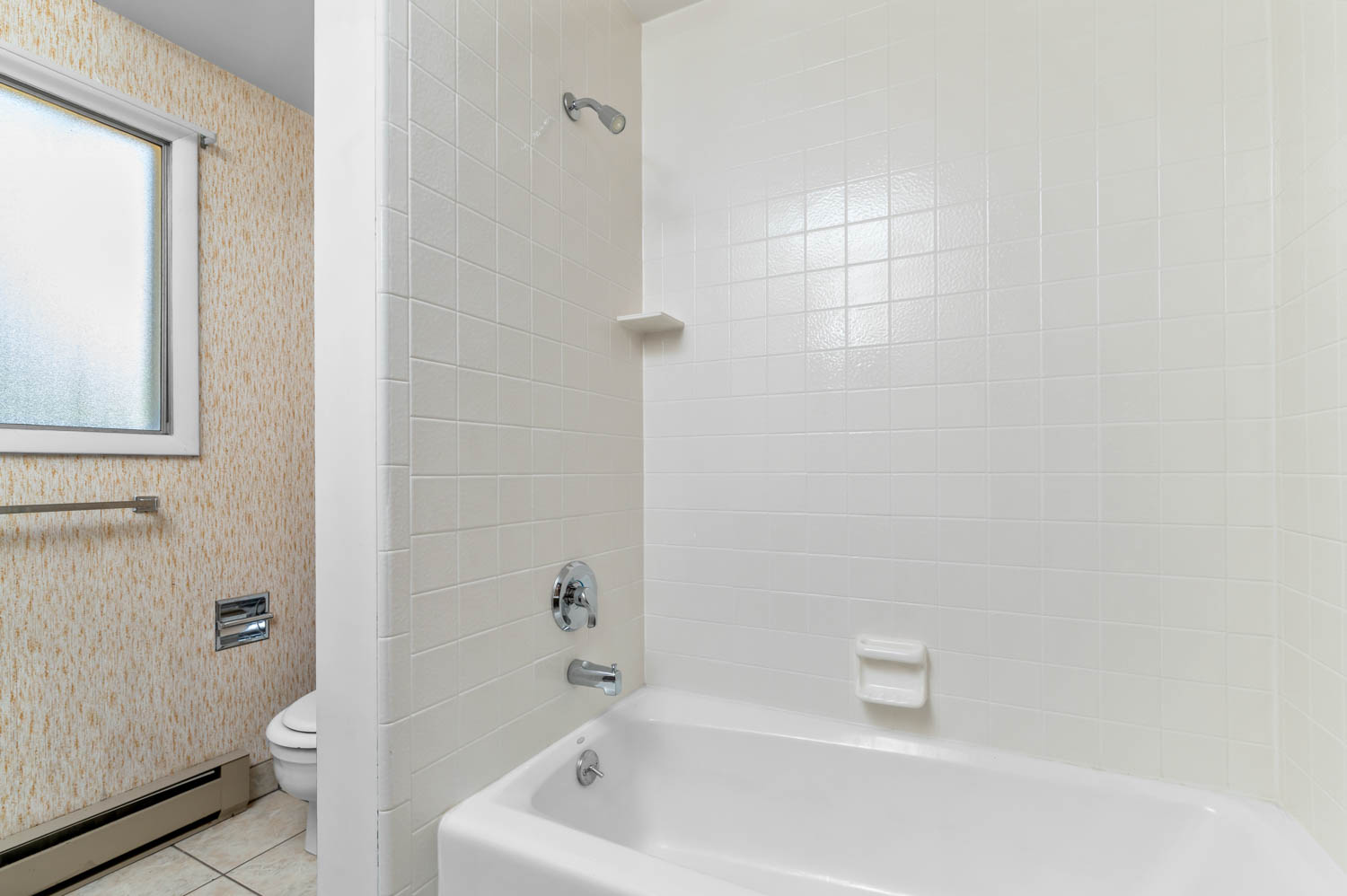White tiled shower surround with a built-in shelf and chrome fixtures, featuring a white tub