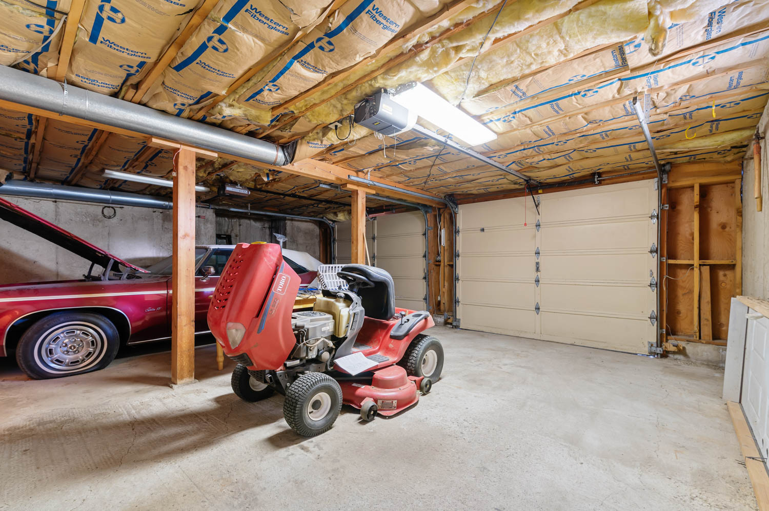 Spacious garage featuring a concrete floor, exposed wood beam ceiling, and multiple garage doors