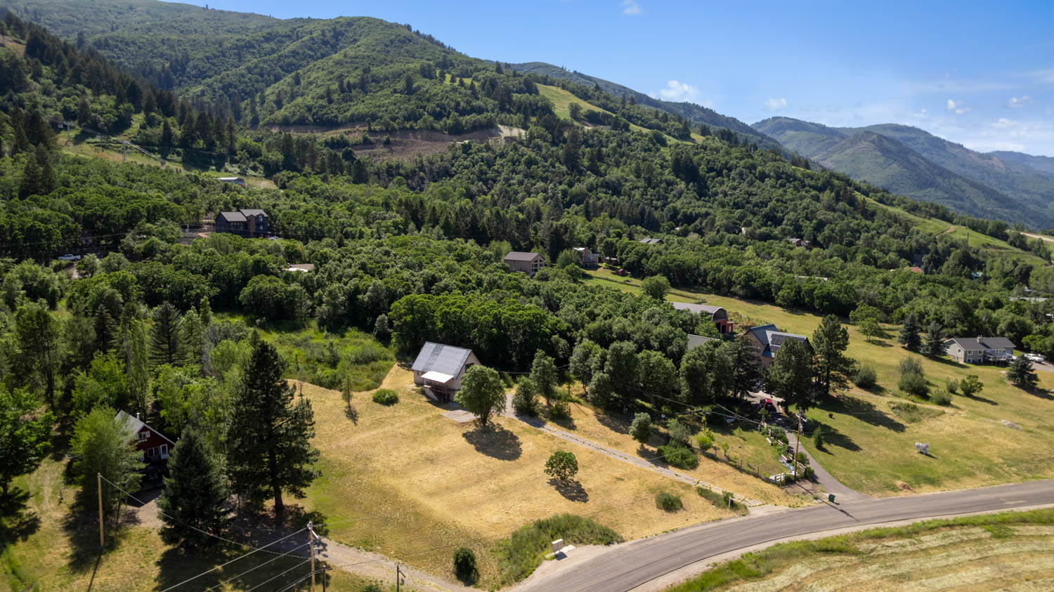 Expansive mountain landscape featuring a winding road and multiple structures nestled among lush trees and natural terrain