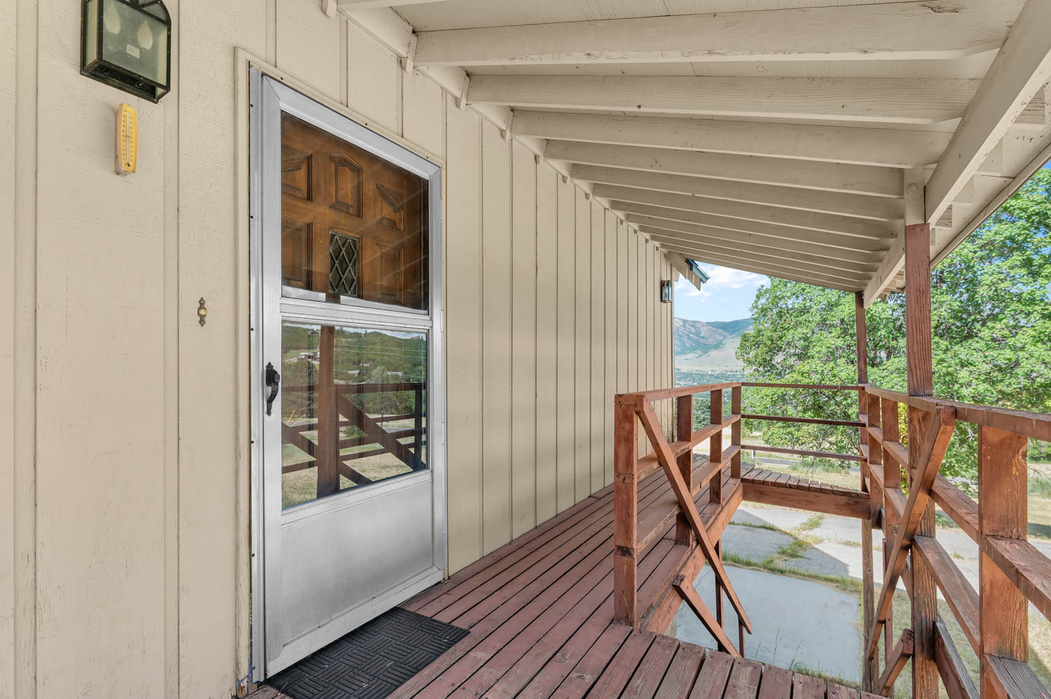 Covered wood-finish porch featuring a full-light storm door, exterior lighting fixture, vertical siding, and a wooden railing system with integrated stairs