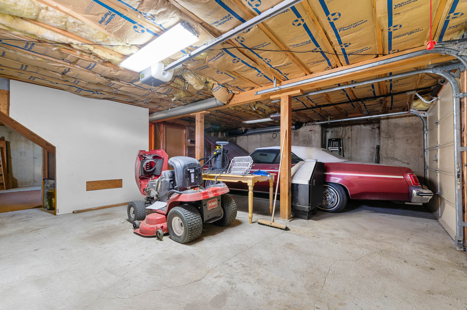 Spacious garage with concrete flooring, exposed ceiling insulation, fluorescent lighting, and an overhead garage door