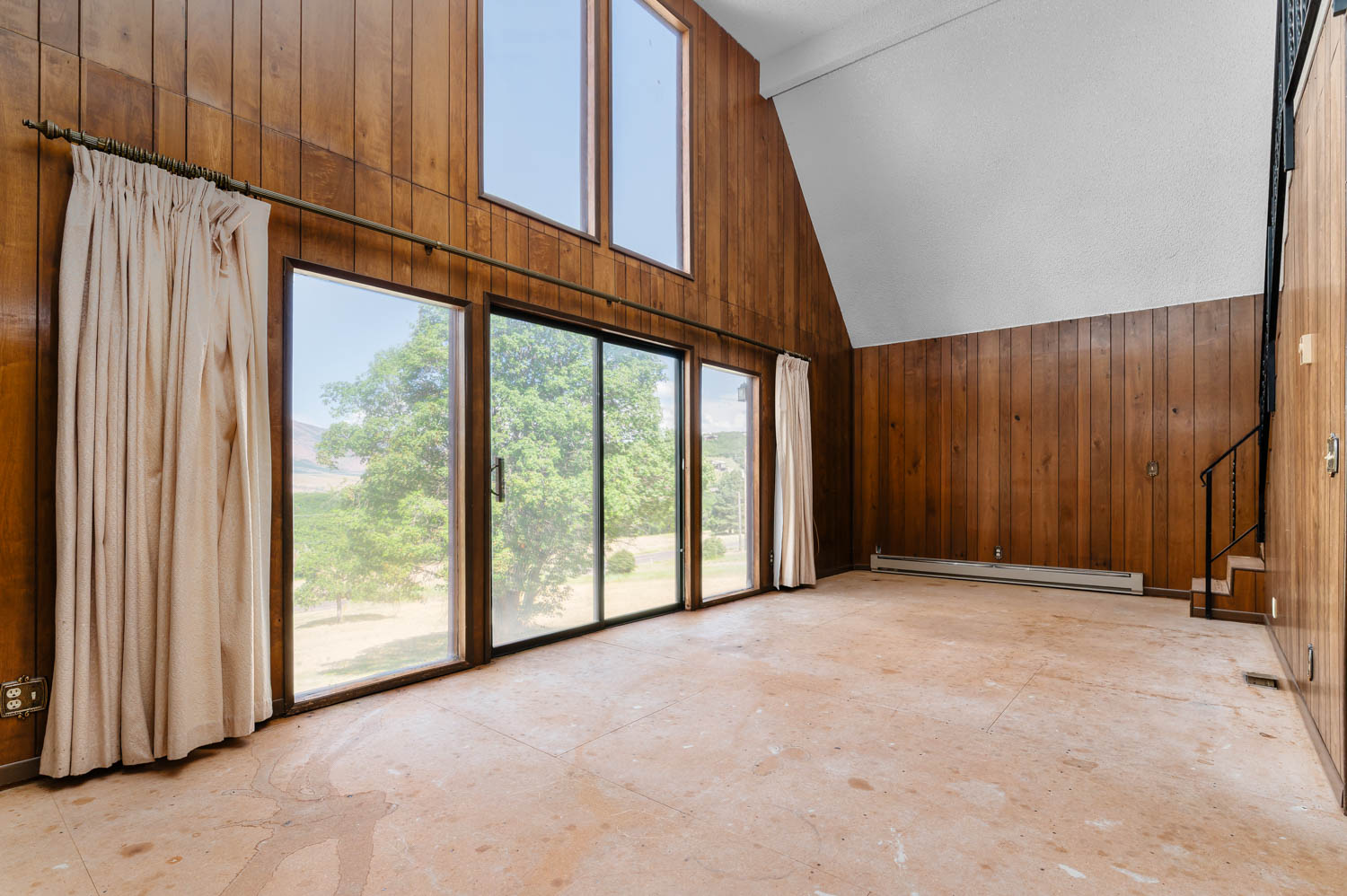 Spacious living area featuring extensive wood paneling, a vaulted ceiling, and large sliding glass doors