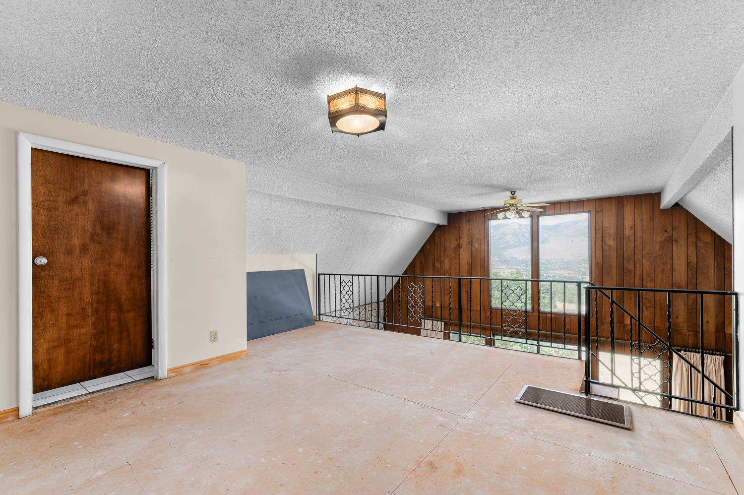 Open loft area featuring a wood-paneled accent wall, a ceiling fan, and large windows