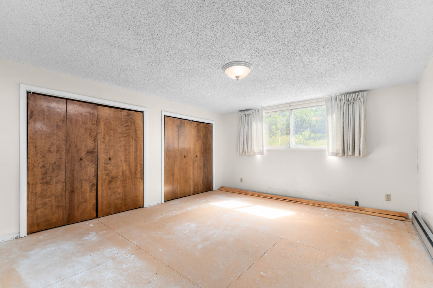 Bedroom with two wood-finish bi-fold closets, broad window, and a flush mount ceiling light fixture