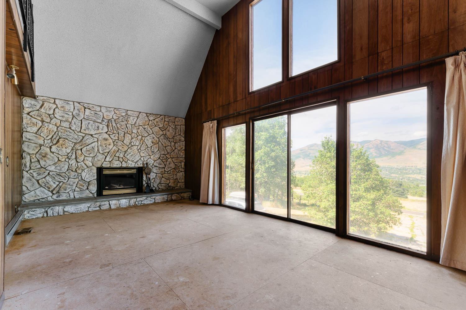 Spacious room featuring a stone-clad fireplace with hearth, expansive floor-to-ceiling windows, and additional upper transom windows