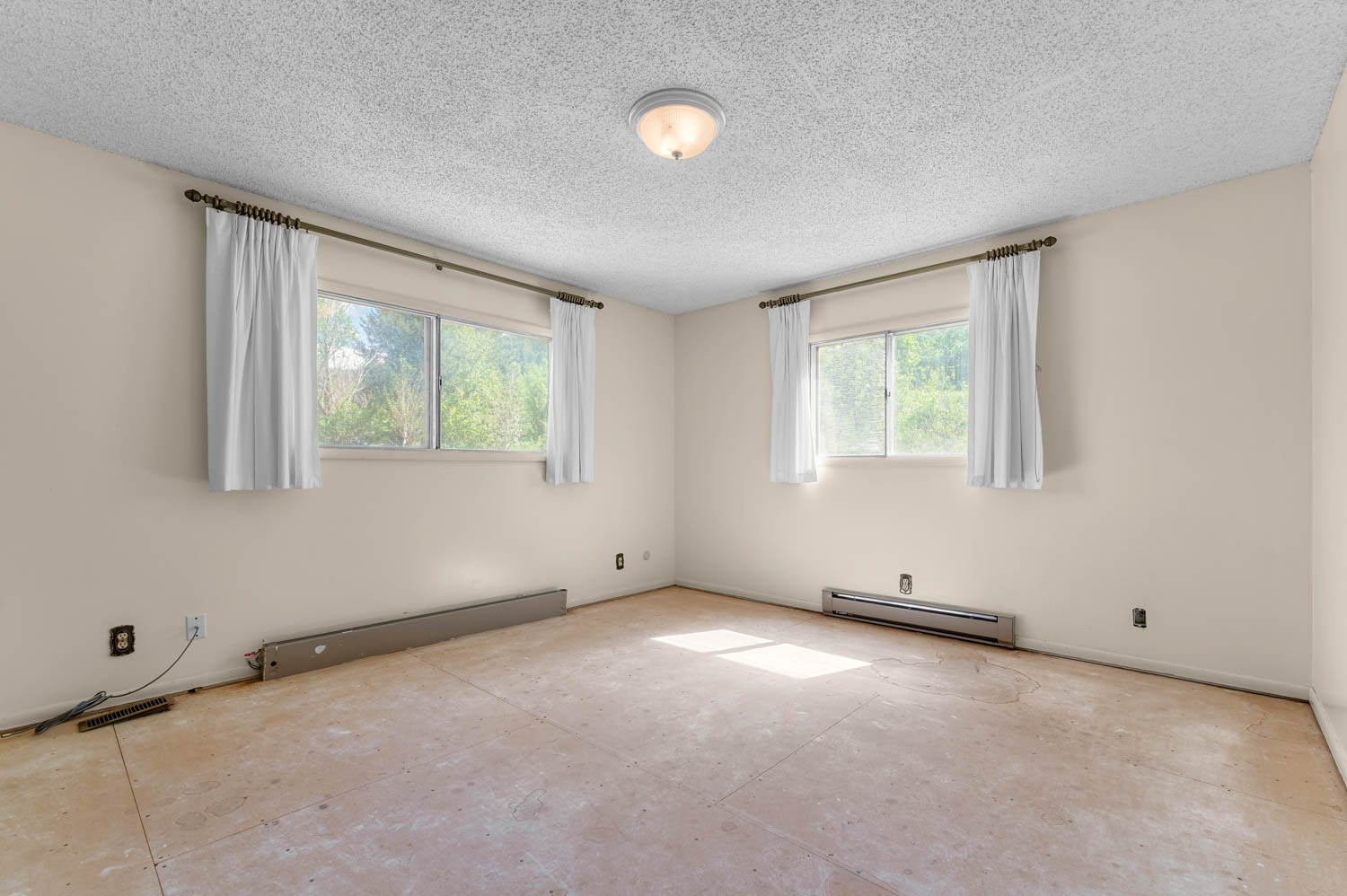 Spacious room featuring two large windows with natural light, light-toned walls, and a textured ceiling
