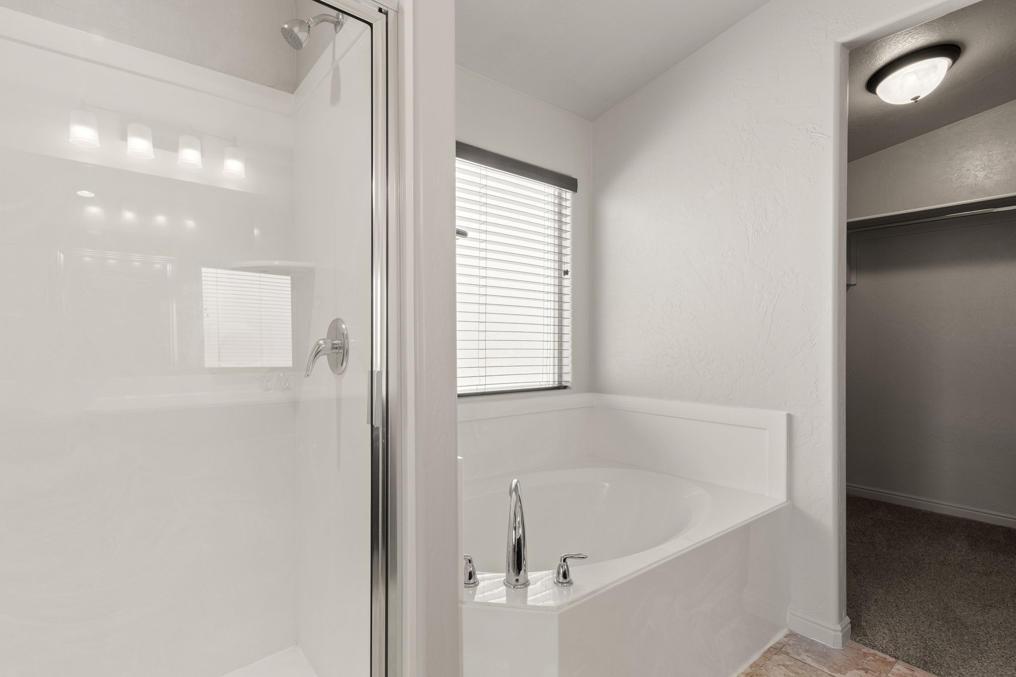 Bathroom featuring a corner soaking tub with chrome fixtures, a separate shower with a clear glass enclosure and chrome showerhead, and a window with blinds