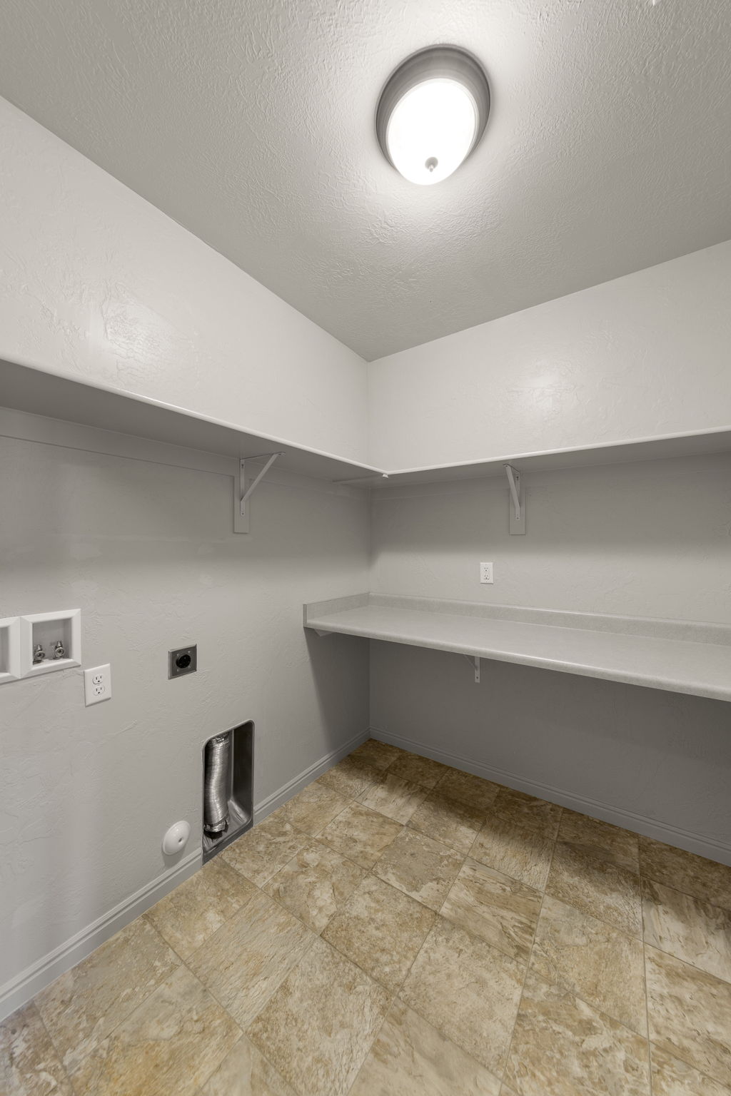 Dedicated utility space featuring a neutral color palette, integrated wall shelving, a built-in countertop, and patterned tile flooring